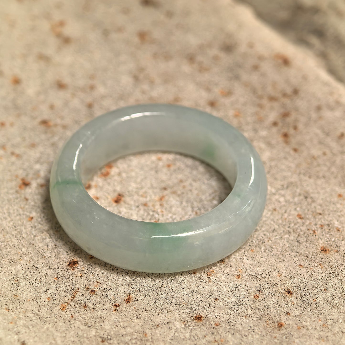 Natural Grade-A light green jadeite ring band displayed on stone, showing its rounded structure and icy glutinous texture.