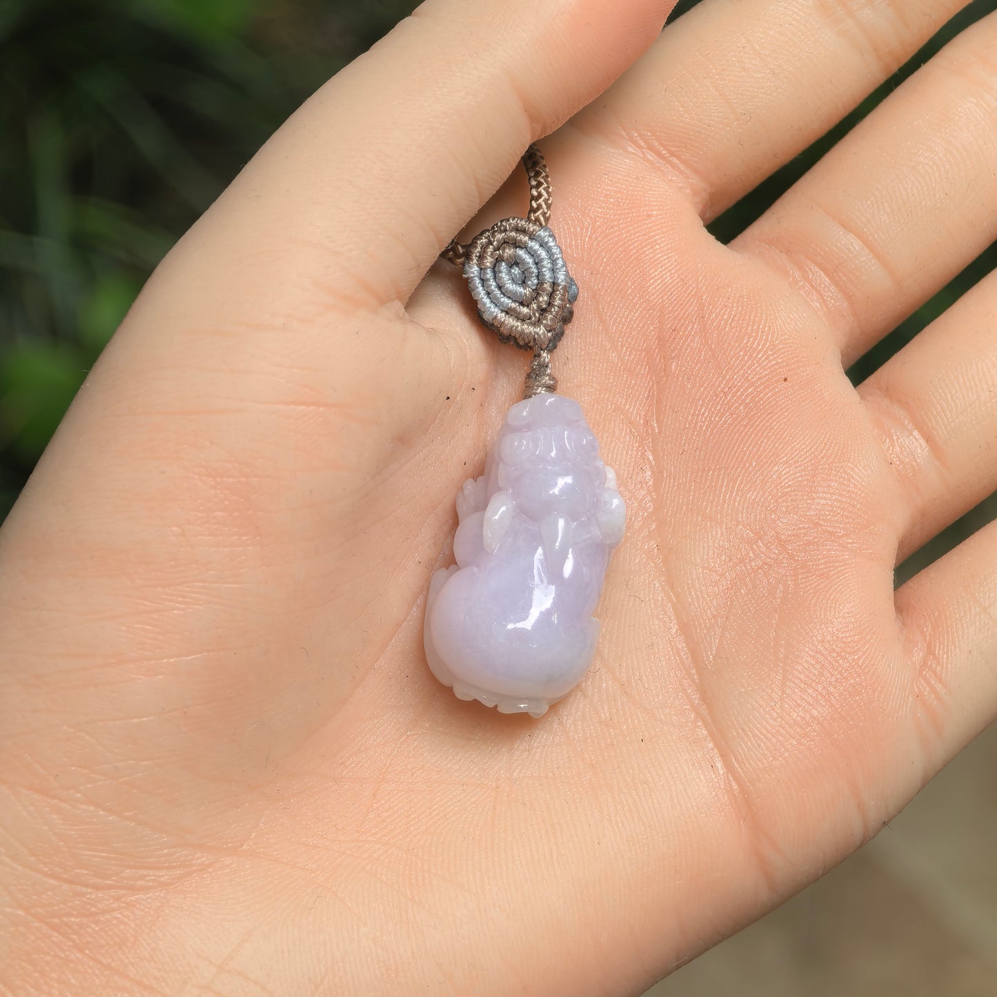 Natural Grade-A glutinous pale lavender Pixiu jadeite pendant displayed in hand with its braided cord.