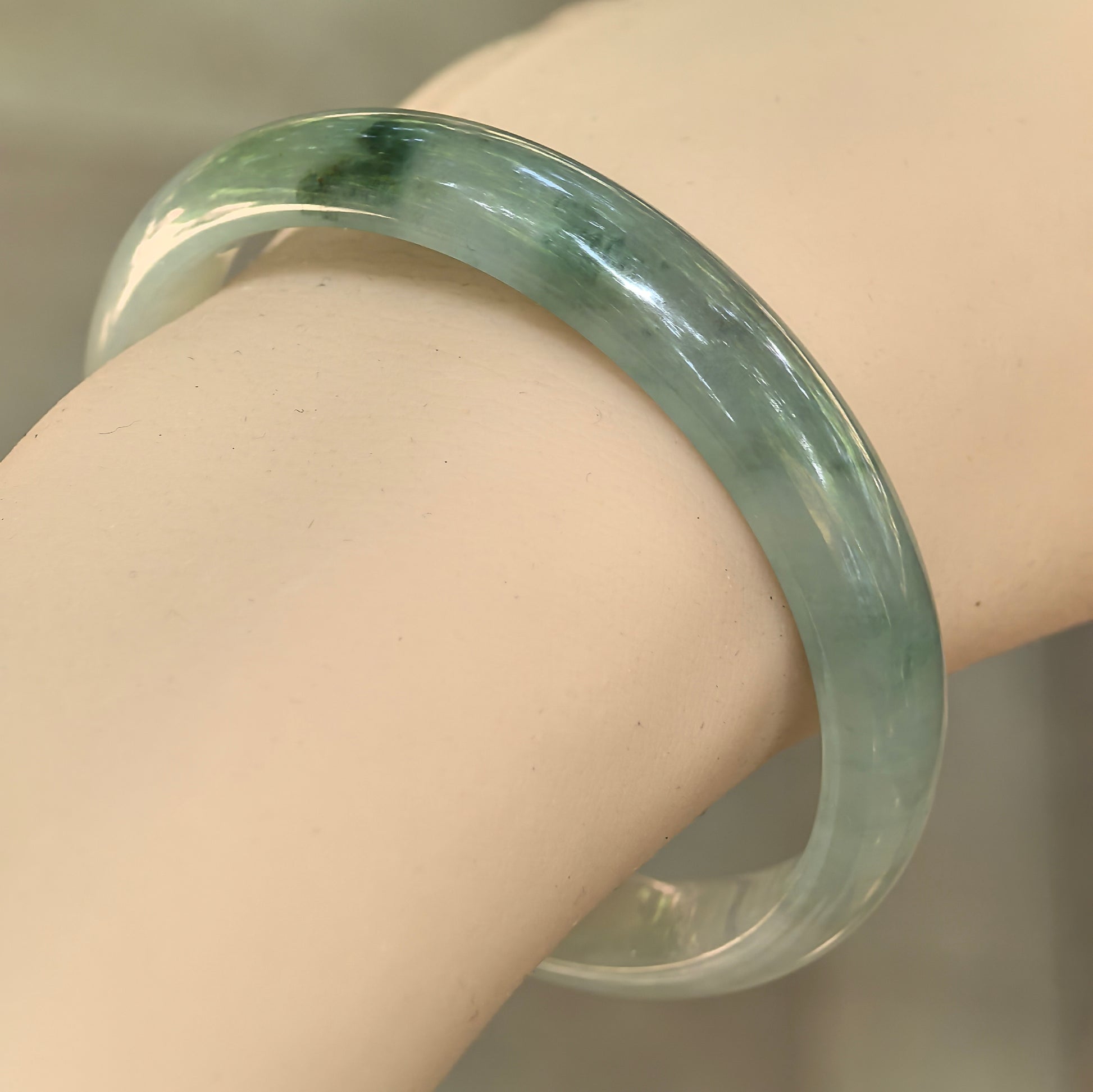 Natural Grade-A icy glutinous light green jadeite D-shape bangle worn on the wrist with dark green floating accents.