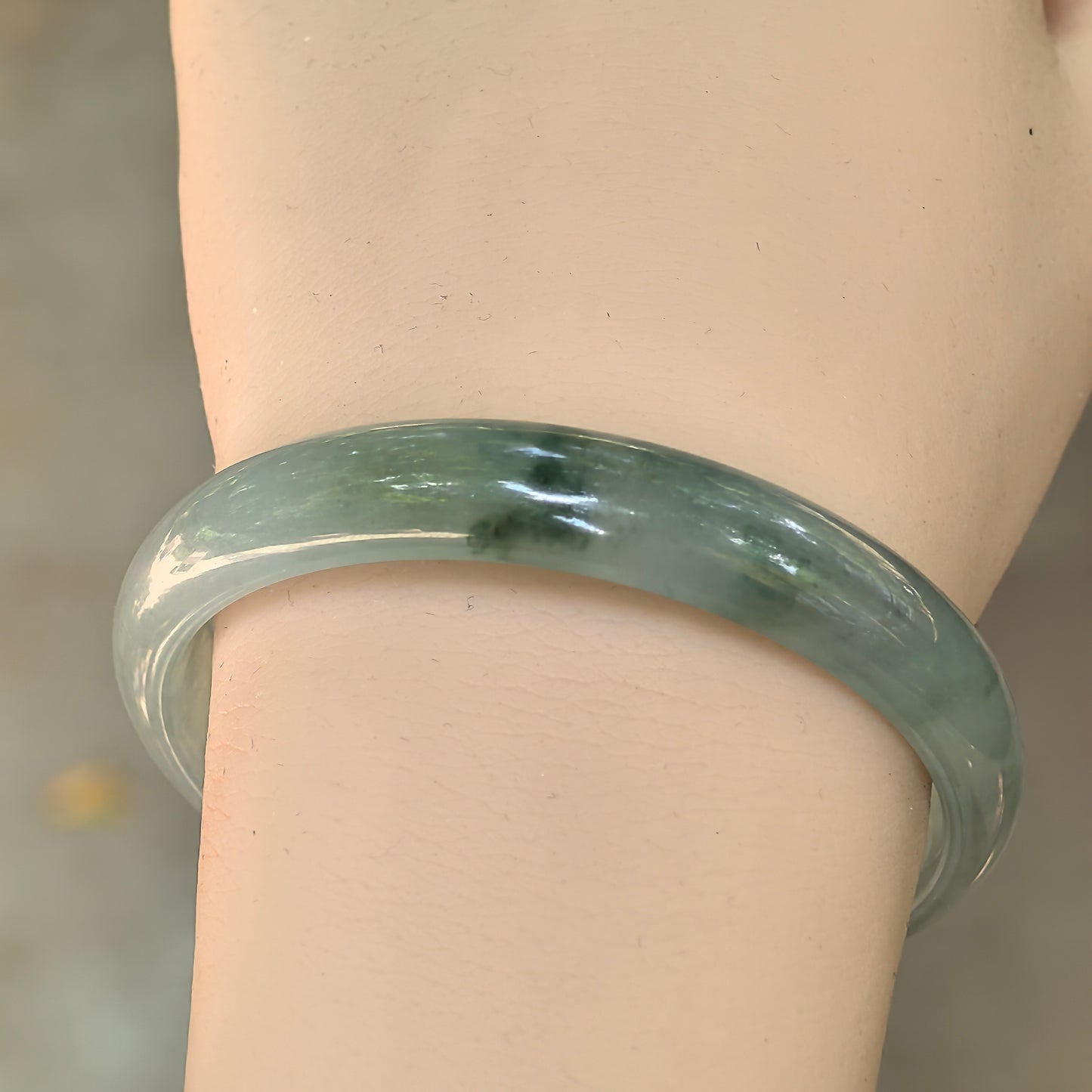 Light green Burmese jadeite bangle worn on the wrist showing good translucency and natural dark green floating patterns.