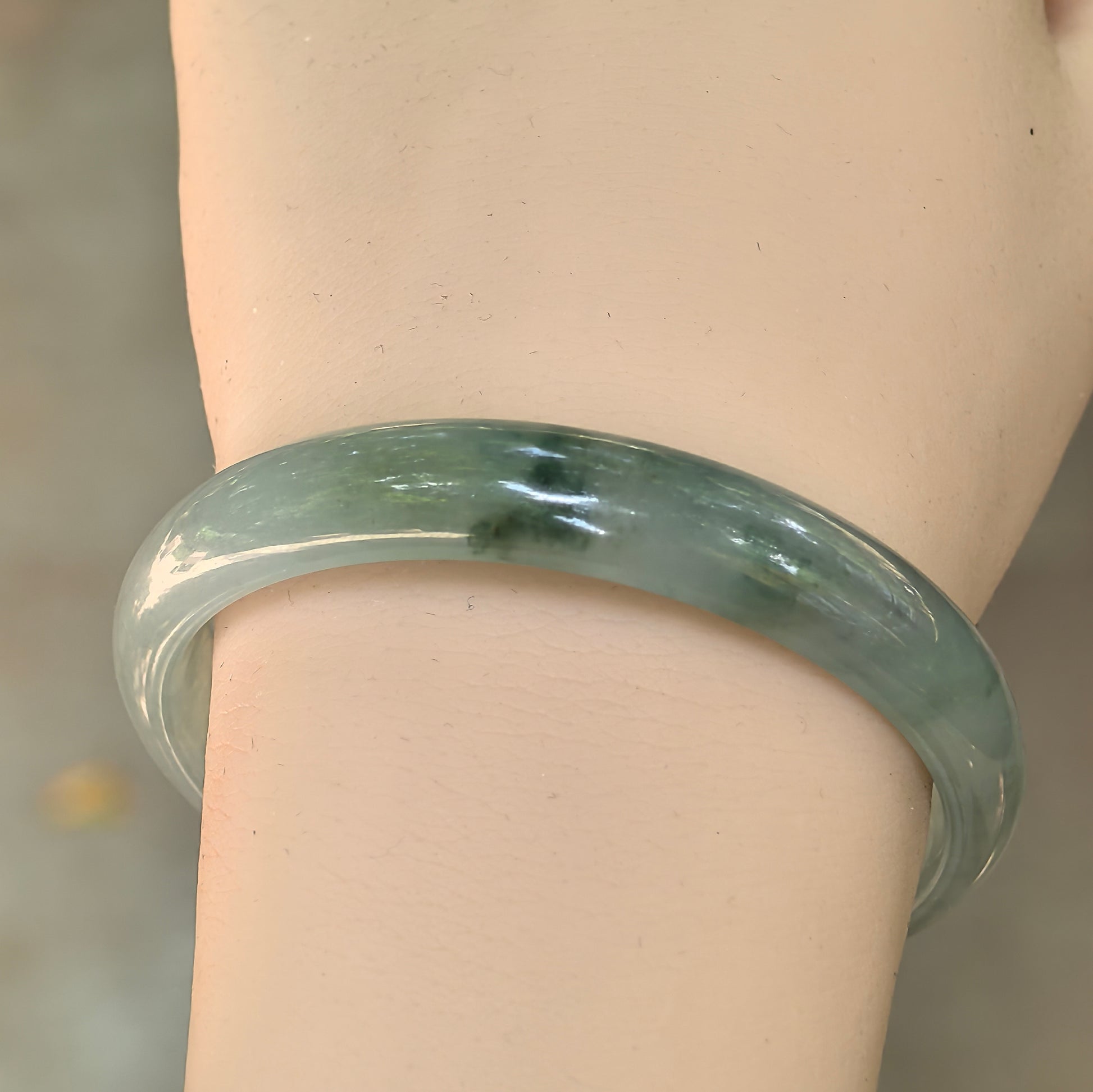 Light green Burmese jadeite bangle worn on the wrist showing good translucency and natural dark green floating patterns.