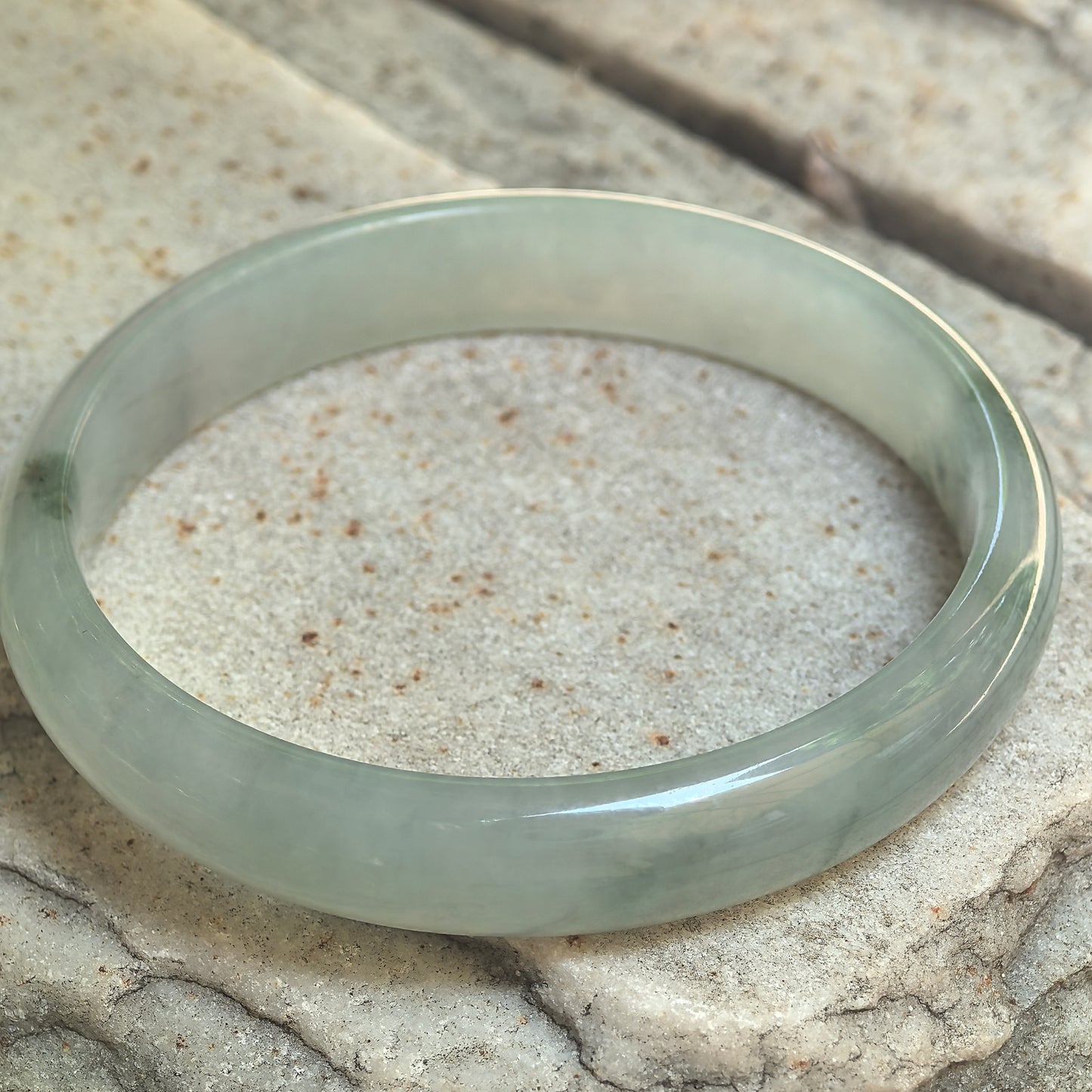 Icy glutinous light green jadeite D-shape bangle displayed on stone showing its slim profile and clean polished surface.