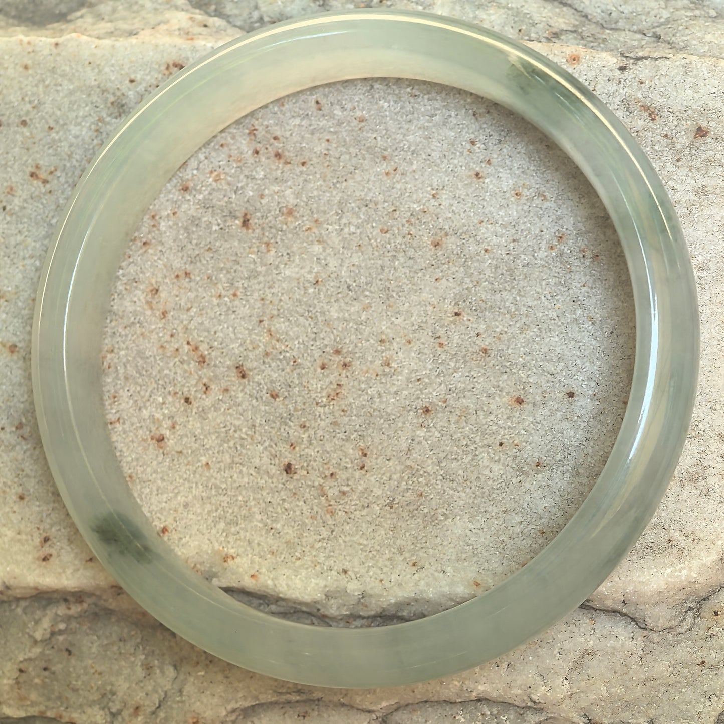 Top view of natural light green jadeite bangle showing the full D-shape form and scattered dark green accents.