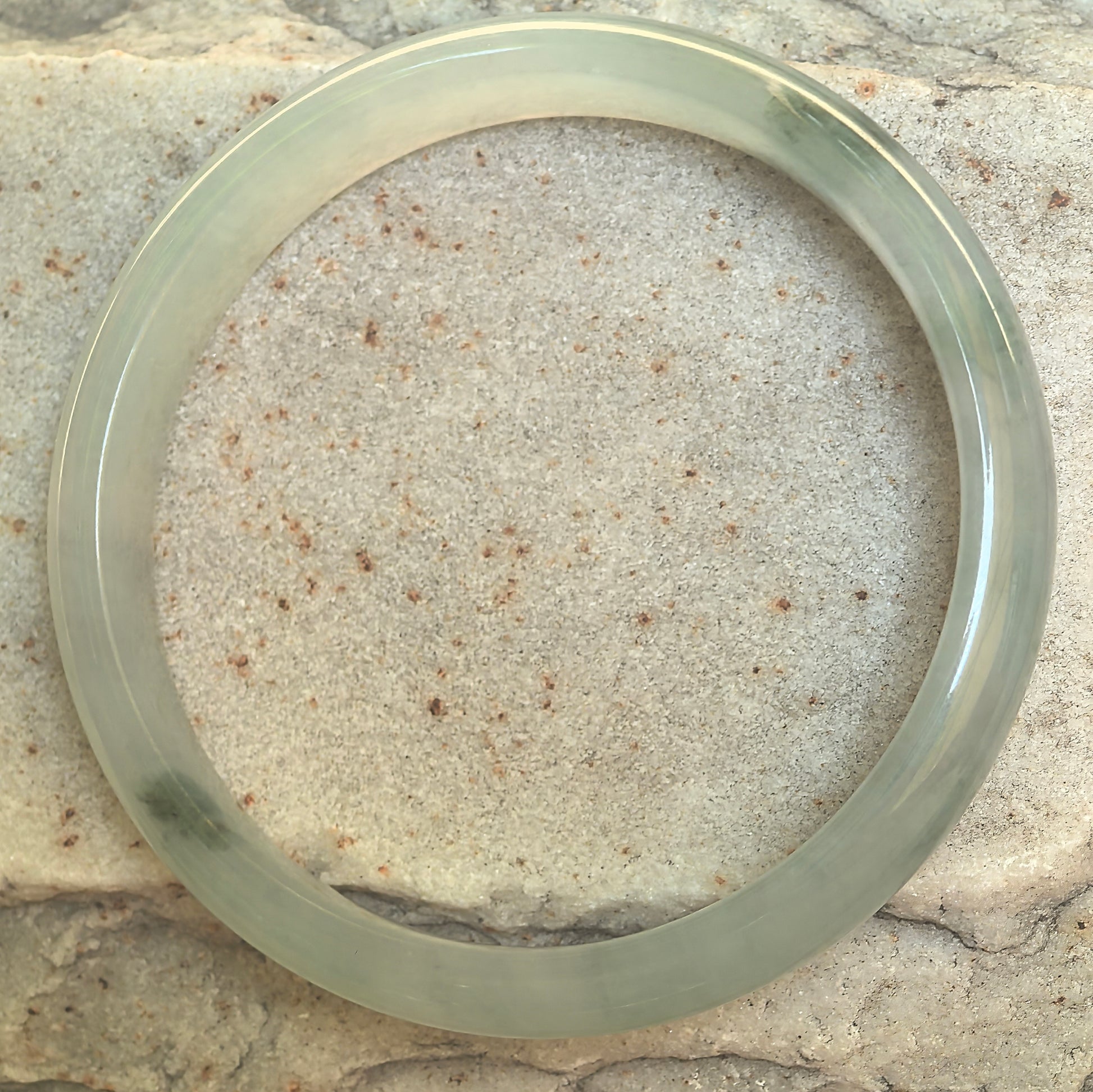 Top view of natural light green jadeite bangle showing the full D-shape form and scattered dark green accents.
