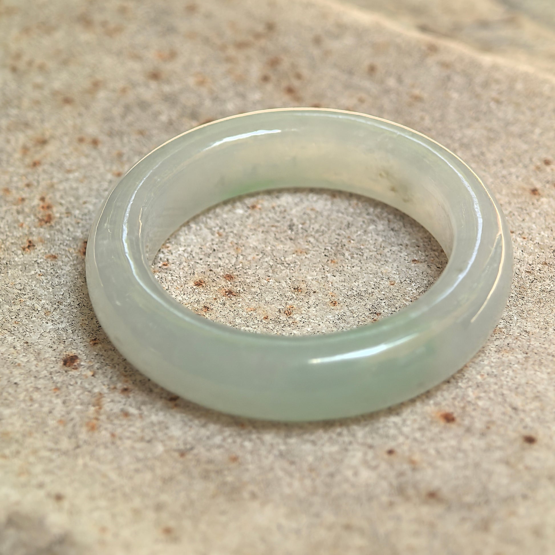 Natural light green jadeite ring band displayed upright, showing its seamless circular structure.