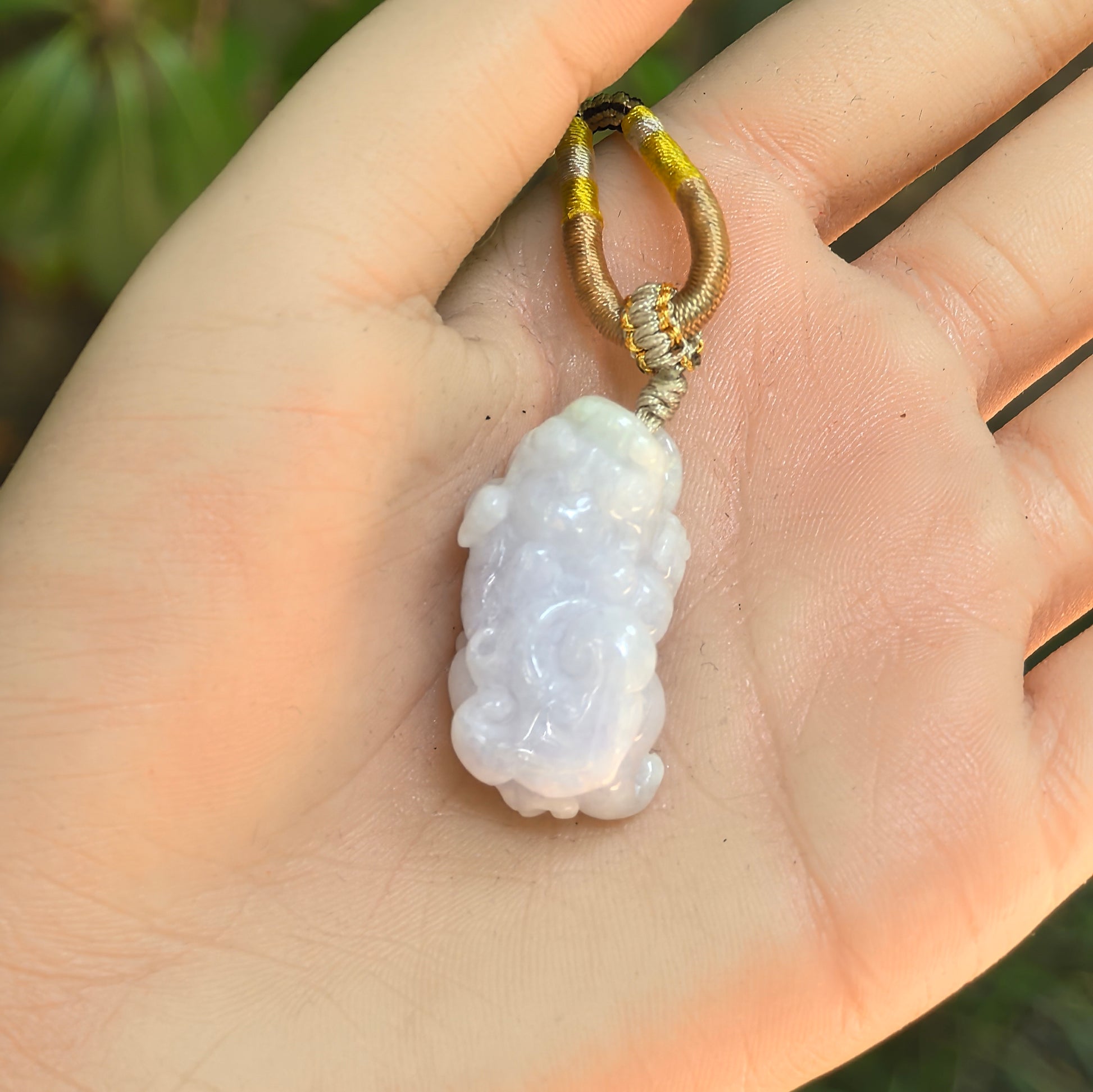 Hand-held pale lavender Pixiu jadeite pendant showing its compact three-dimensional carving.