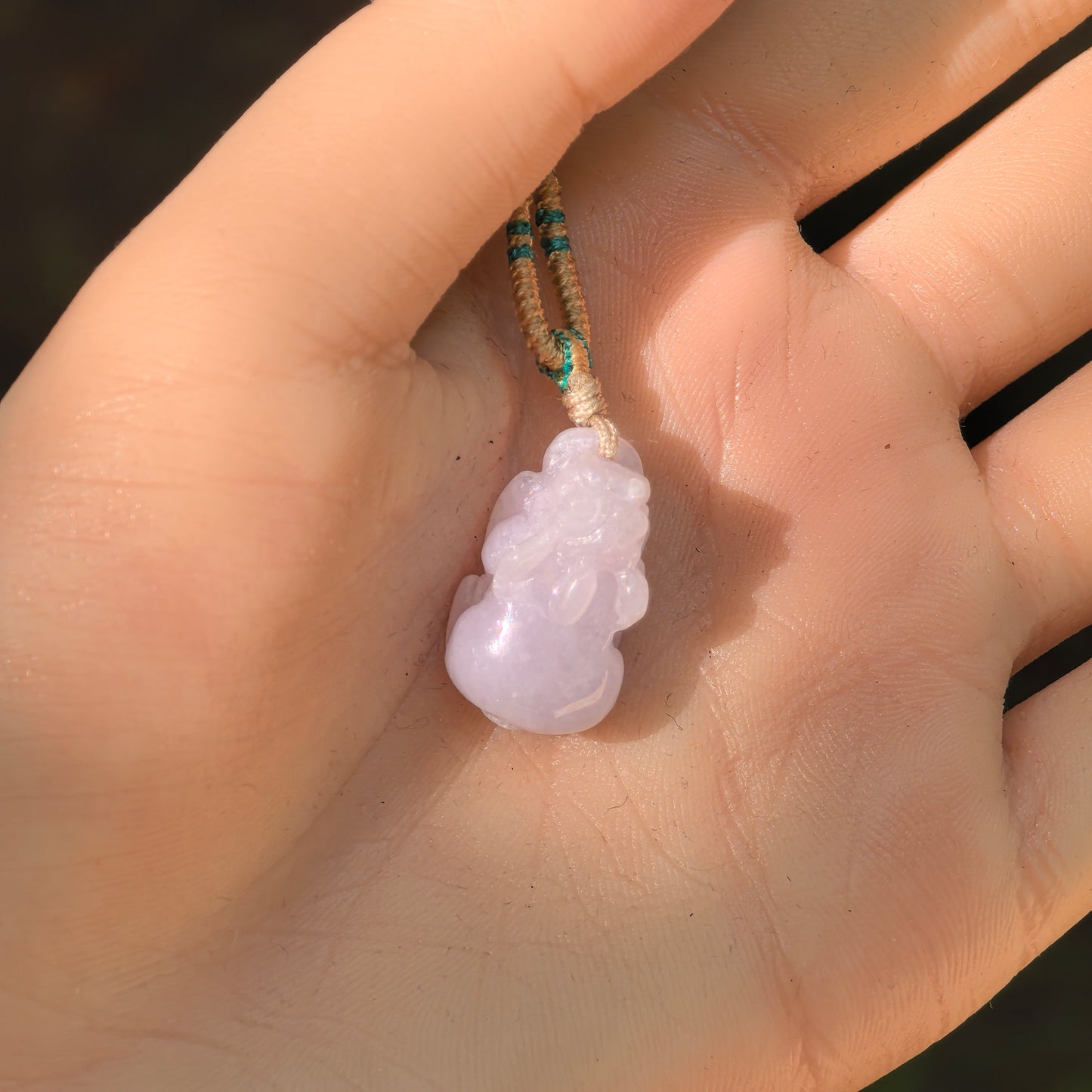 Pale lavender Pixiu jadeite pendant held in the hand, showing its petite size, natural color, and glutinous texture.
