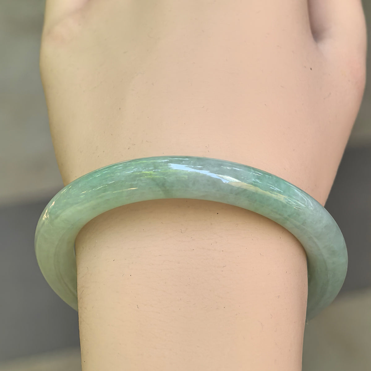 Close-up wrist view of a mint green Burmese jadeite round bangle with translucent icy glutinous texture.