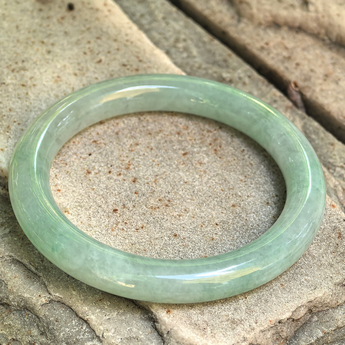 Natural Grade-A mint green jadeite round bangle displayed on stone, showing its polished surface and soft translucency.