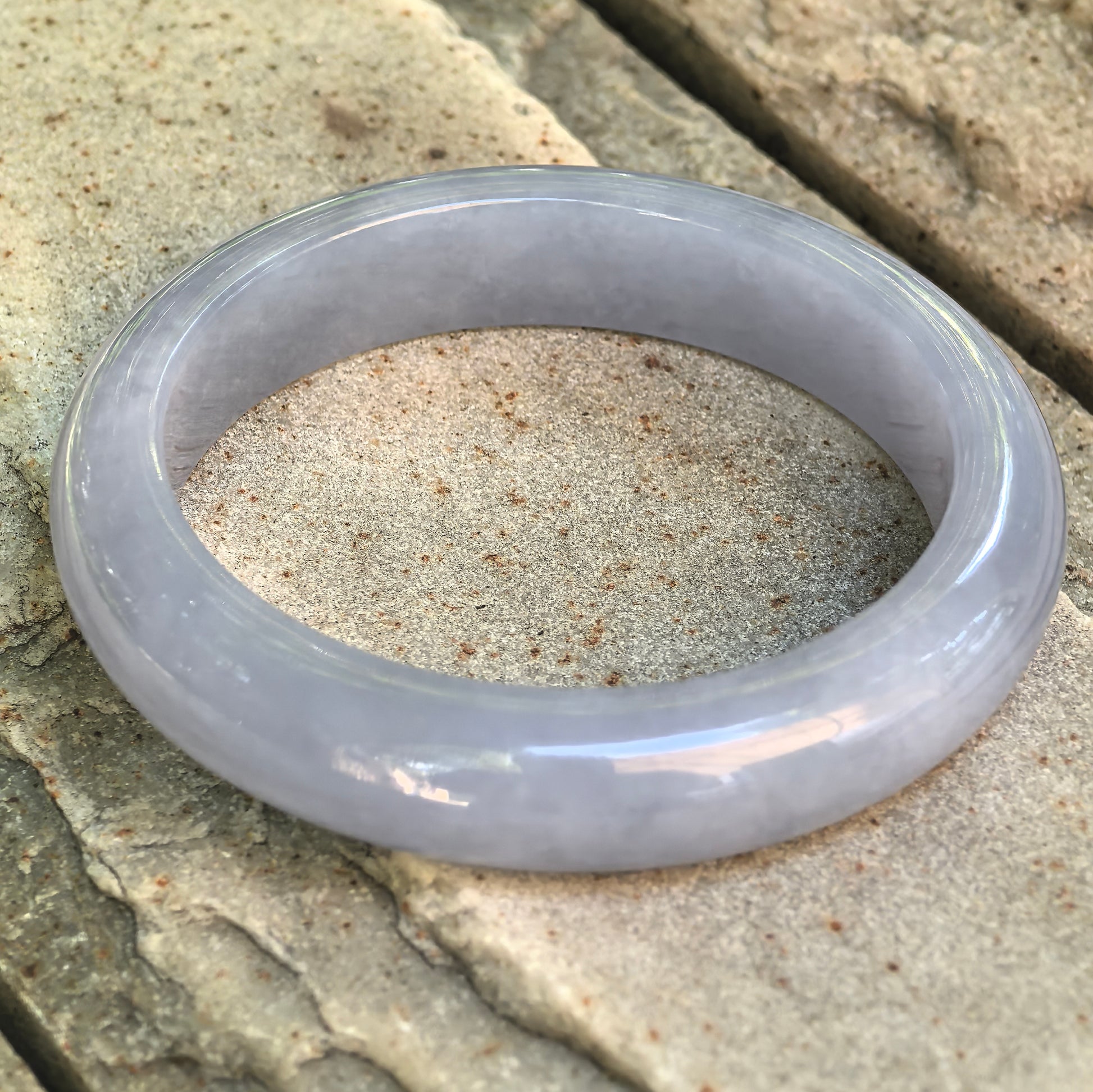 Natural Grade-A lavender-blue Burmese jadeite D-shape bangle displayed at an angle on stone, highlighting its polished surface and full profile.