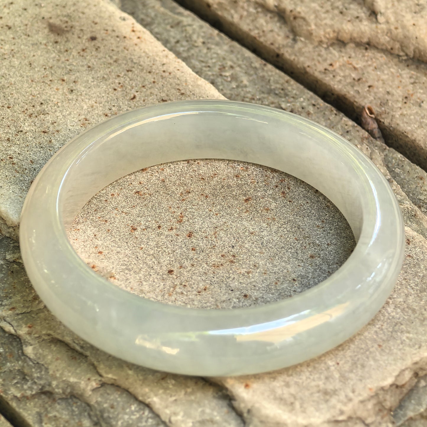 Natural Grade-A glutinous icy white jadeite D-shape bangle shown at an angle on stone, displaying its translucent body and polished finish.