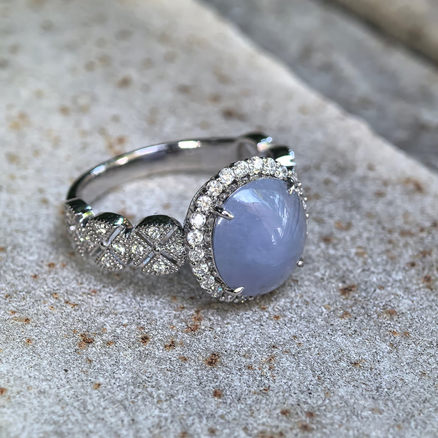 Angled side view of a natural lavender jadeite ring showing the oval cabochon, platinum setting, diamond halo, and openwork details.