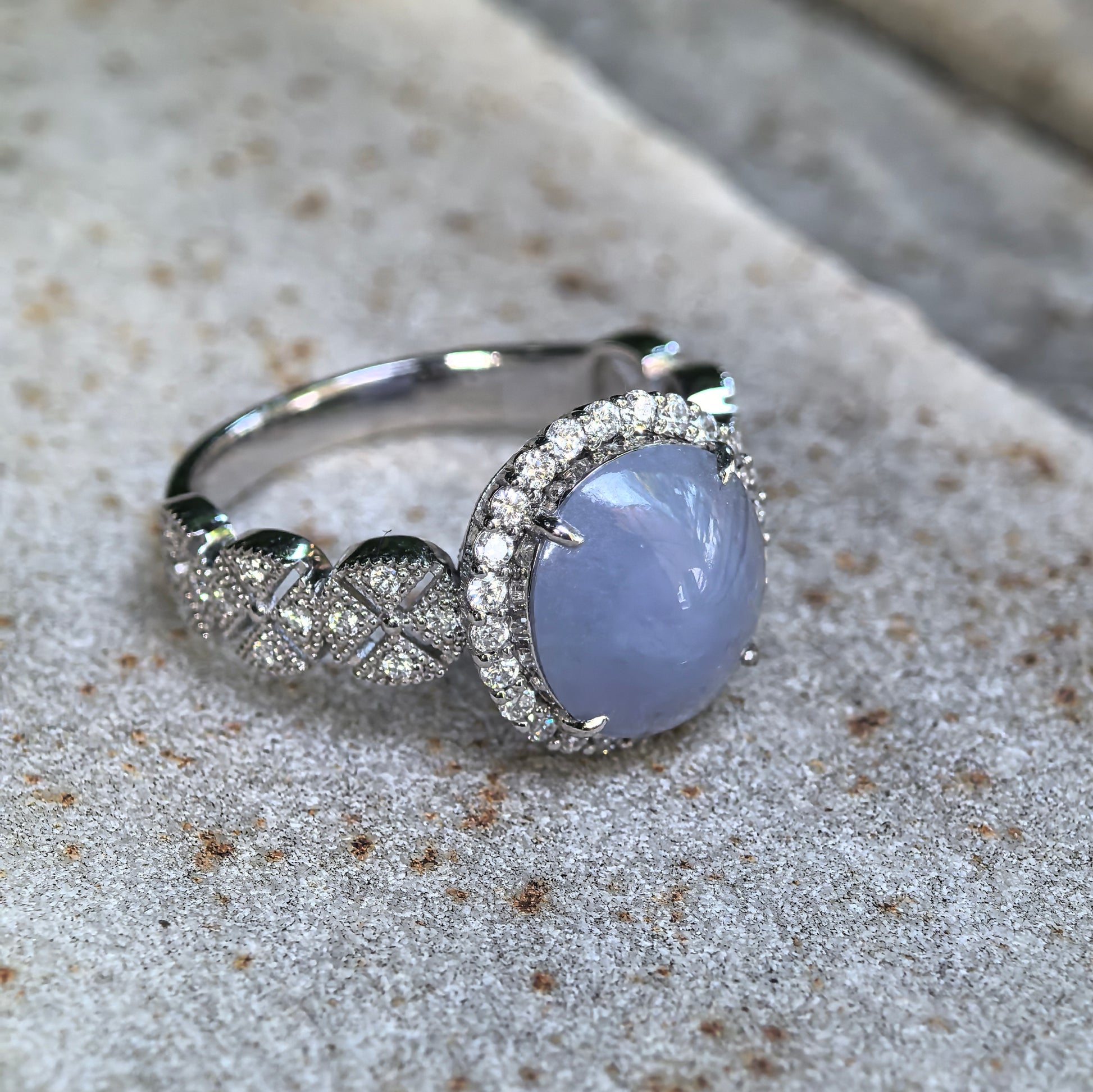 Angled side view of a natural lavender jadeite ring showing the oval cabochon, platinum setting, diamond halo, and openwork details.