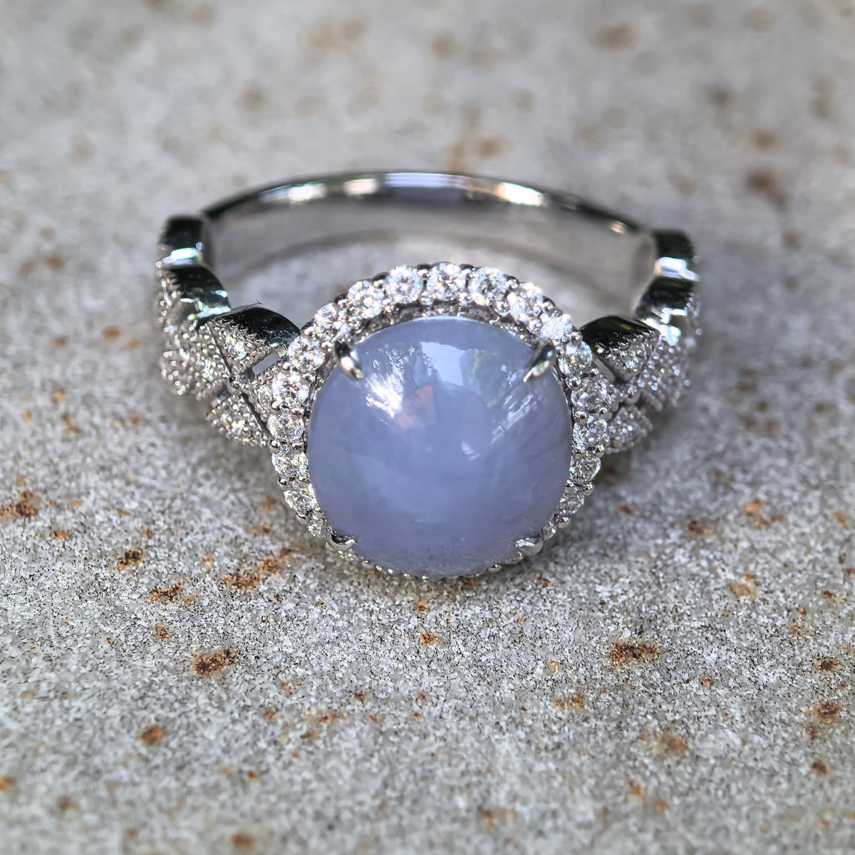 Front display view of a Grade-A purple jadeite cabochon ring with an ornate synthetic diamond halo and floral cluster shoulders.