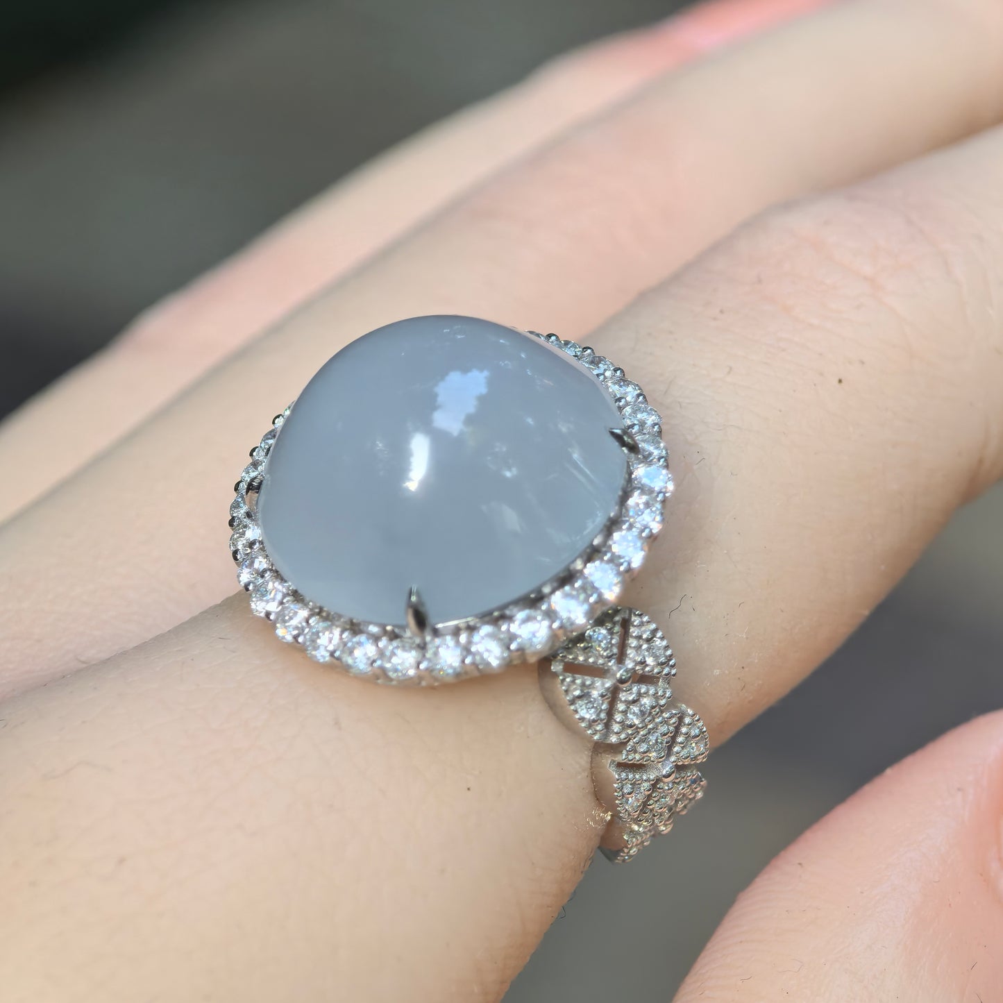 Side wearing view of a natural light blue jadeite ring showing the high-domed cabochon, Pt950 platinum setting, and diamond halo.