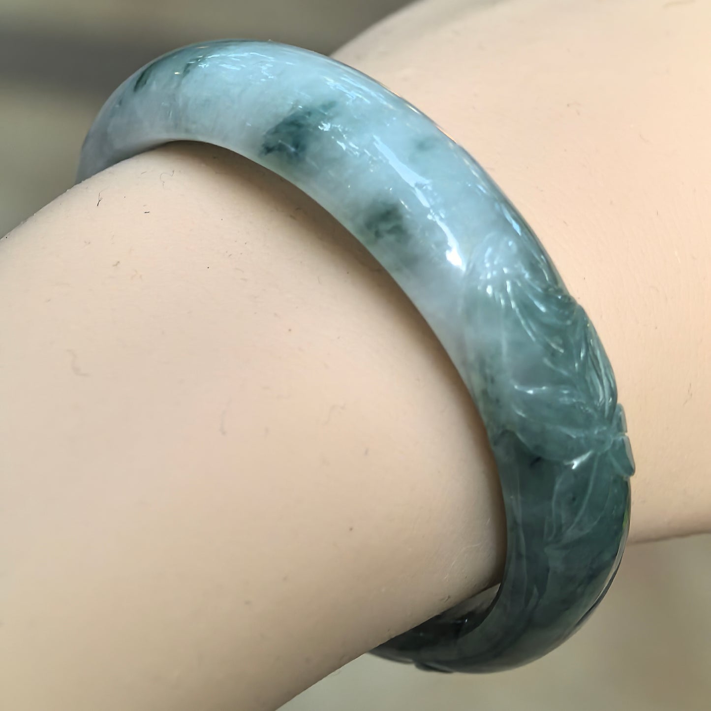 Natural Grade-A glutinous green floating flower carved oval jadeite bangle worn on the wrist, showing its polished surface and relief carving.