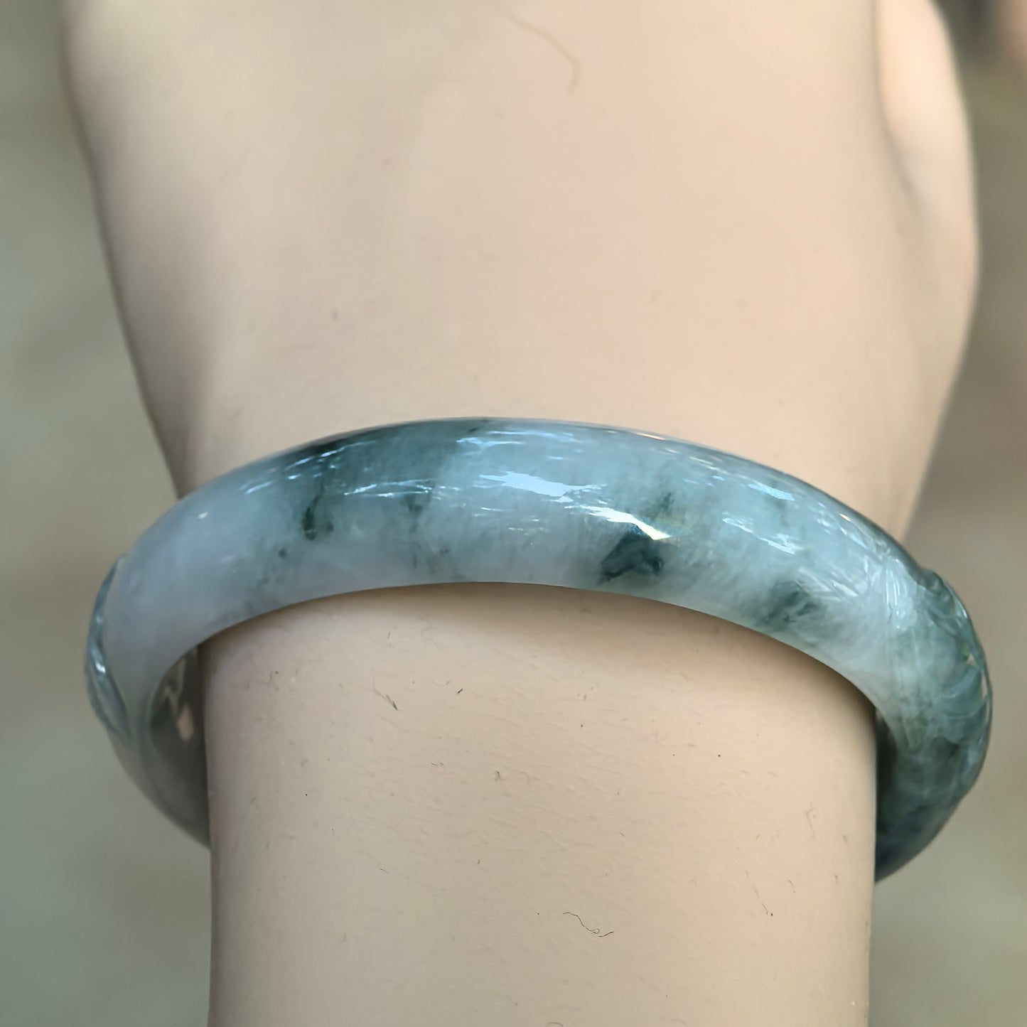 Wrist view of a green floating flower Burmese jadeite oval bangle showing darker natural green patterns and smooth glutinous texture.