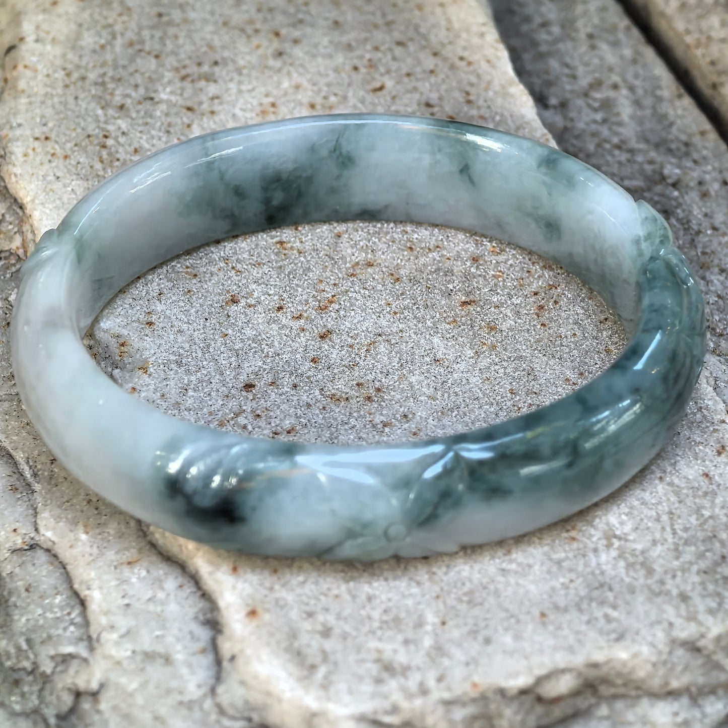 Natural Grade-A green floating flower carved jadeite bangle displayed on stone, showing decorative relief carving and an oval profile.
