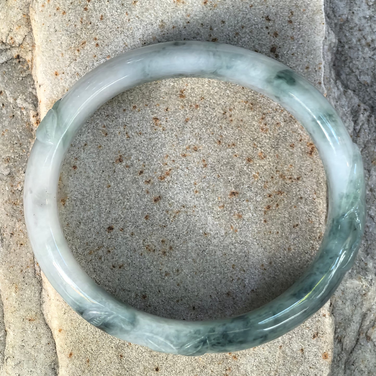 Top view of a glutinous green Burmese jadeite oval bangle showing natural floating-flower patterns and carved decorative sections.