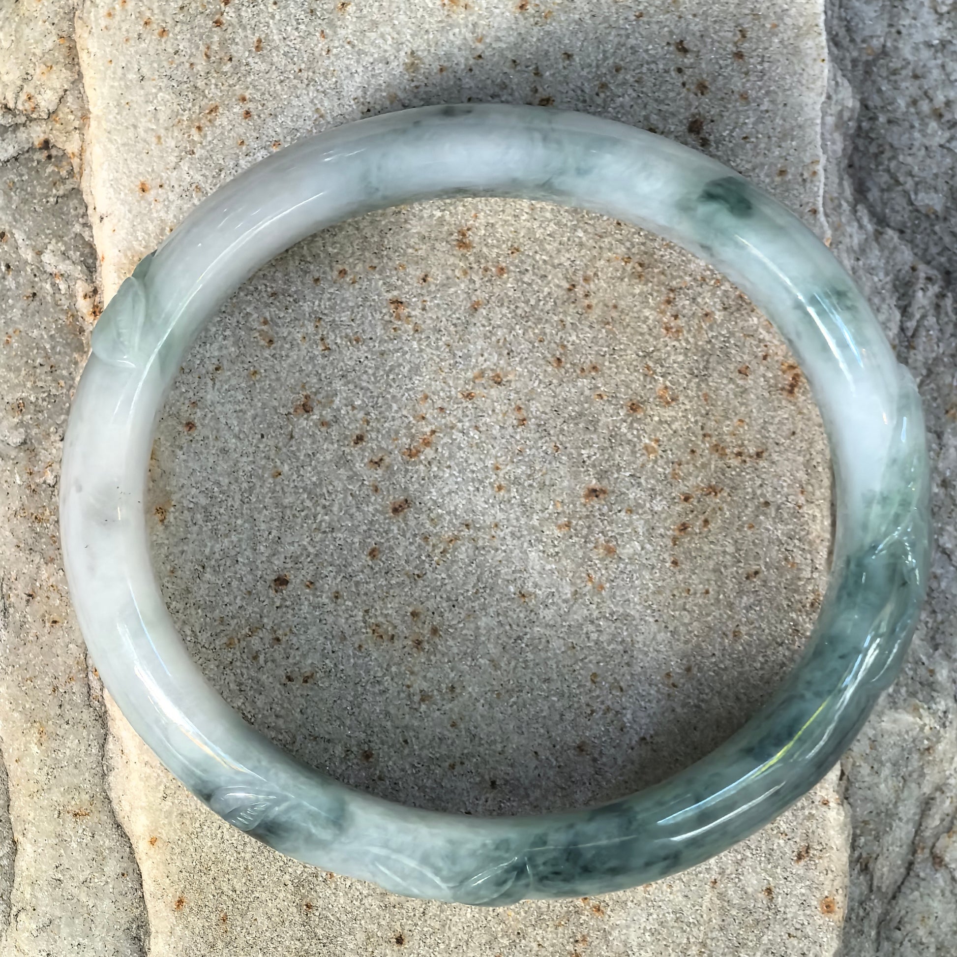 Top view of a glutinous green Burmese jadeite oval bangle showing natural floating-flower patterns and carved decorative sections.