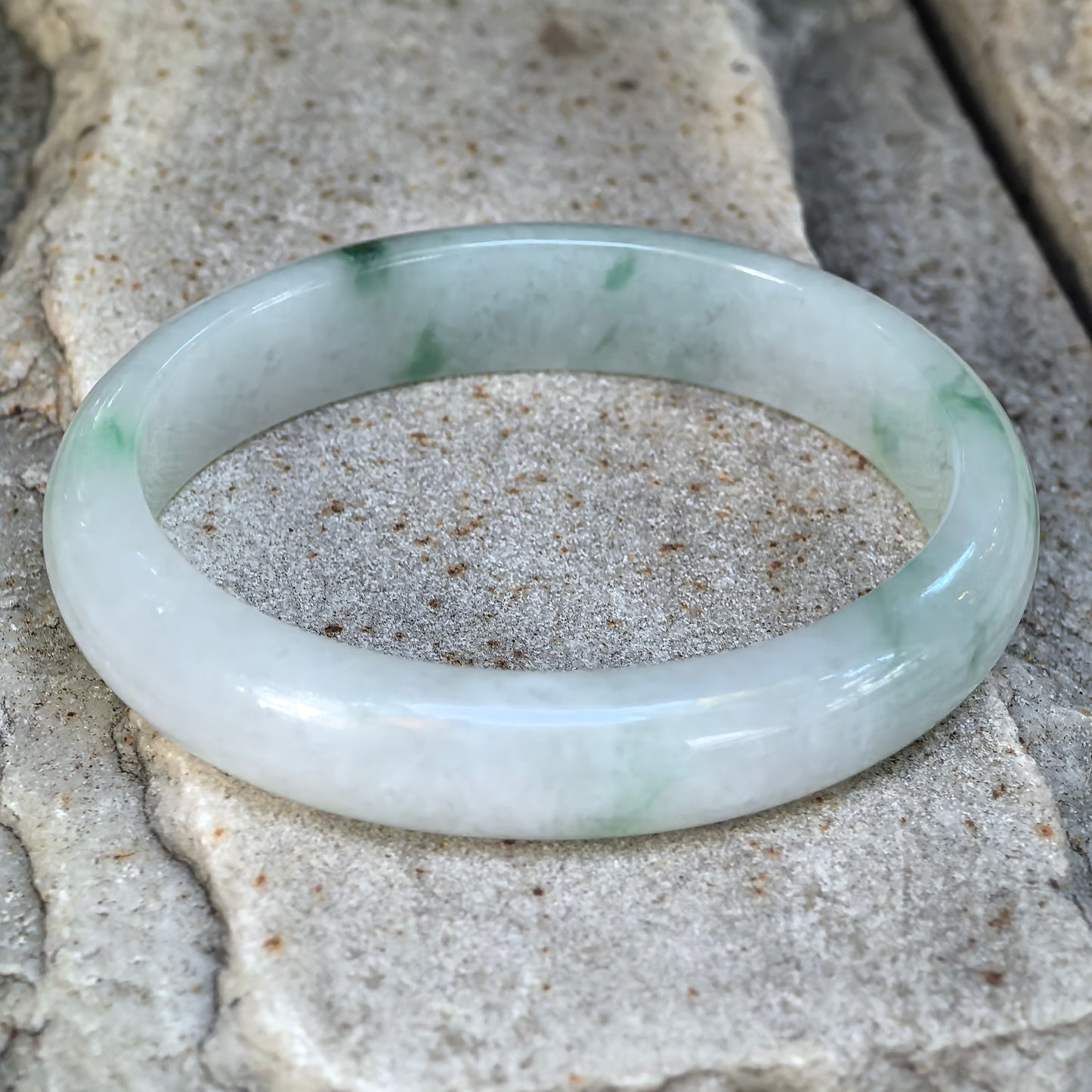 Natural Grade-A fine glutinous green floating flower Burmese jadeite oval bangle shown at an angle, highlighting its pale body and polished luster.