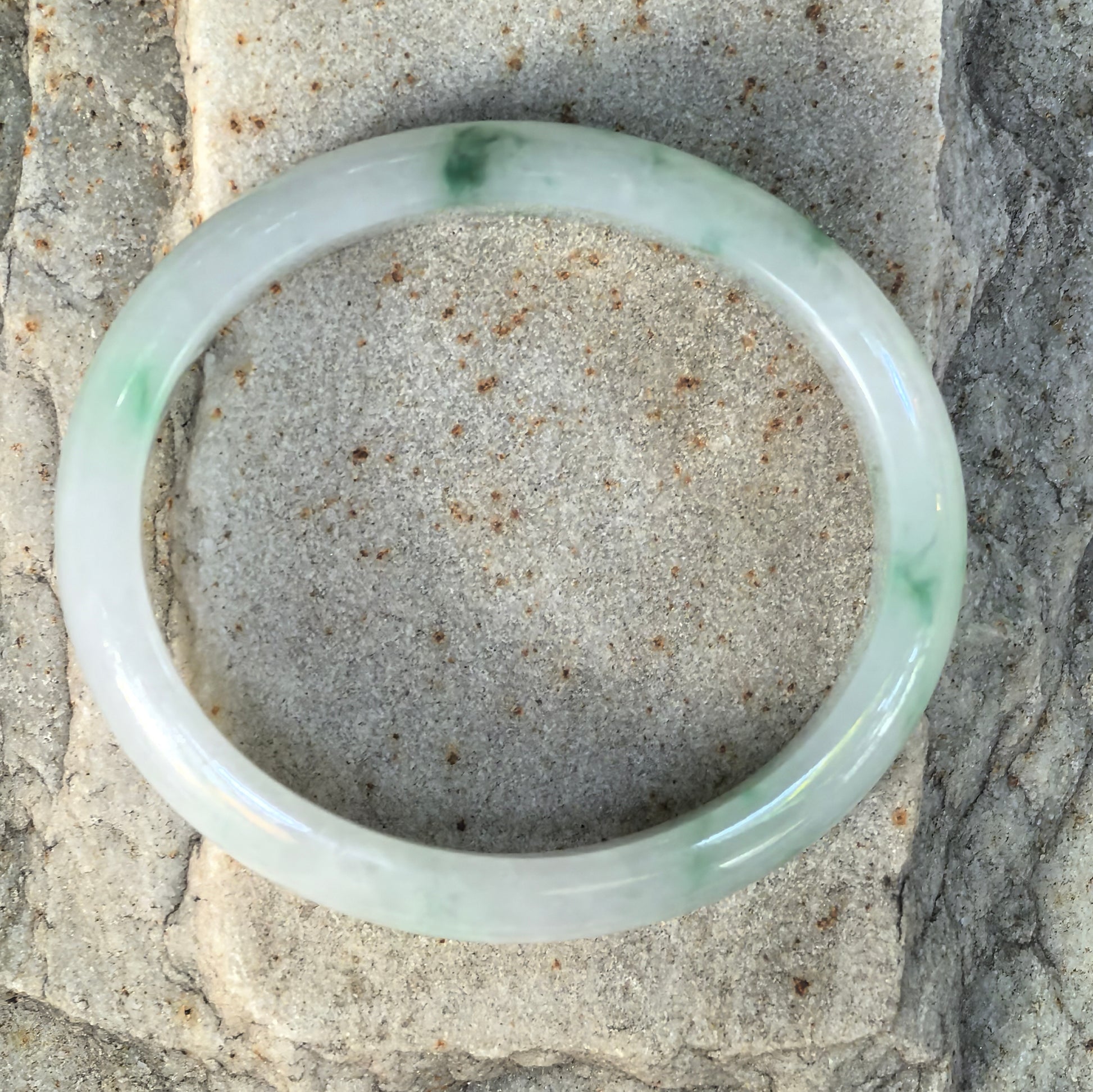 Top view of a fine glutinous green floating flower jadeite oval bangle showing naturally distributed green accents across the pale jadeite body.