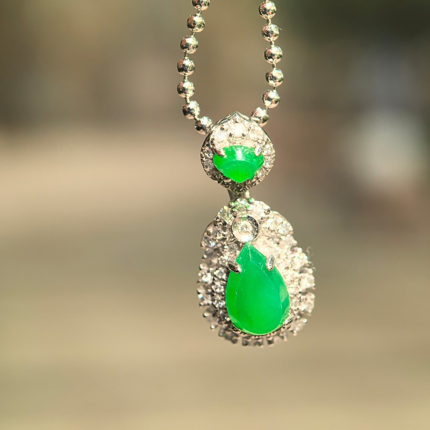 Natural Grade-A icy bright green teardrop jadeite pendant hanging on a chain, showing the layered green jadeite and diamond design.