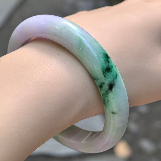 Natural Grade-A glutinous pale lavender and green floating flower jadeite D-shape bangle worn on the wrist, showing vivid green color contrast.