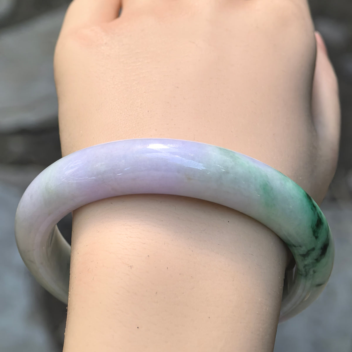 Wrist view of natural Burmese jadeite bangle with pale lavender base and bright green floating flower under natural light.