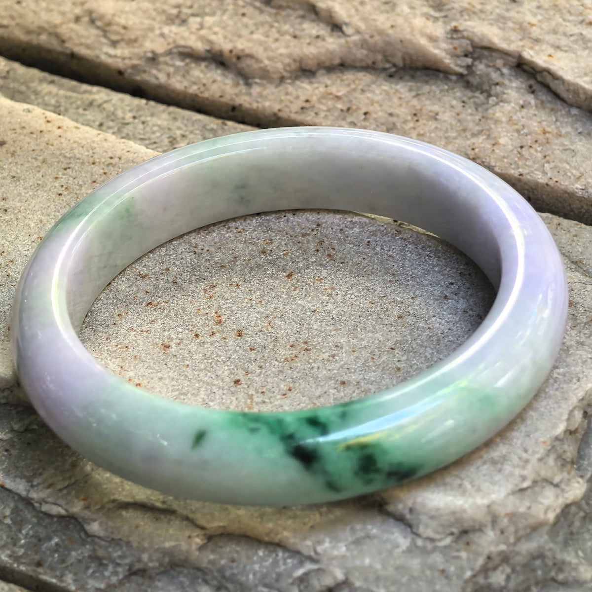 NGTC certified glutinous lavender and green jadeite D-shape bangle displayed on stone, showing the vivid floating flower section.