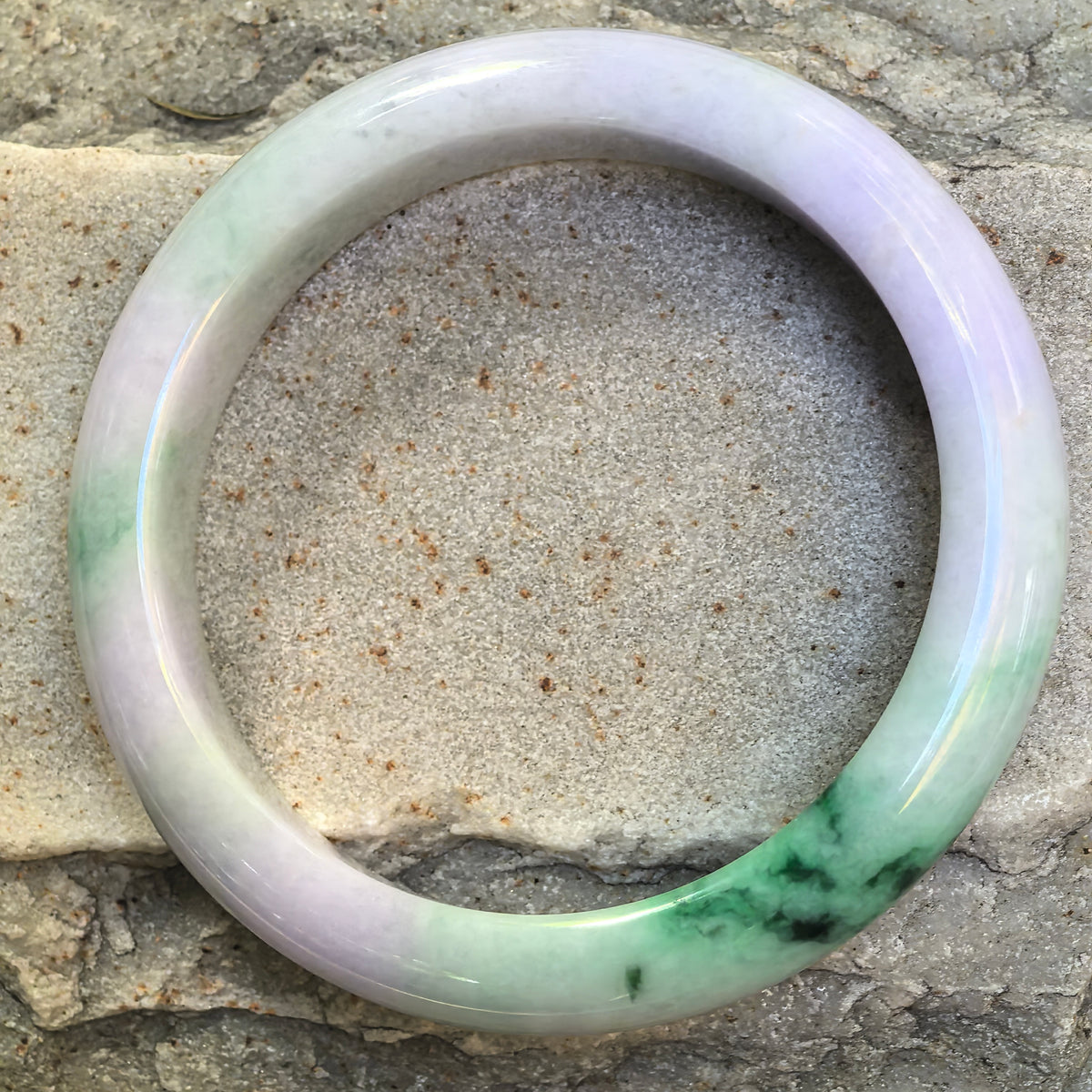 Top view of pale lavender and light green natural jadeite bangle showing smooth D-shape profile and green floating flower.