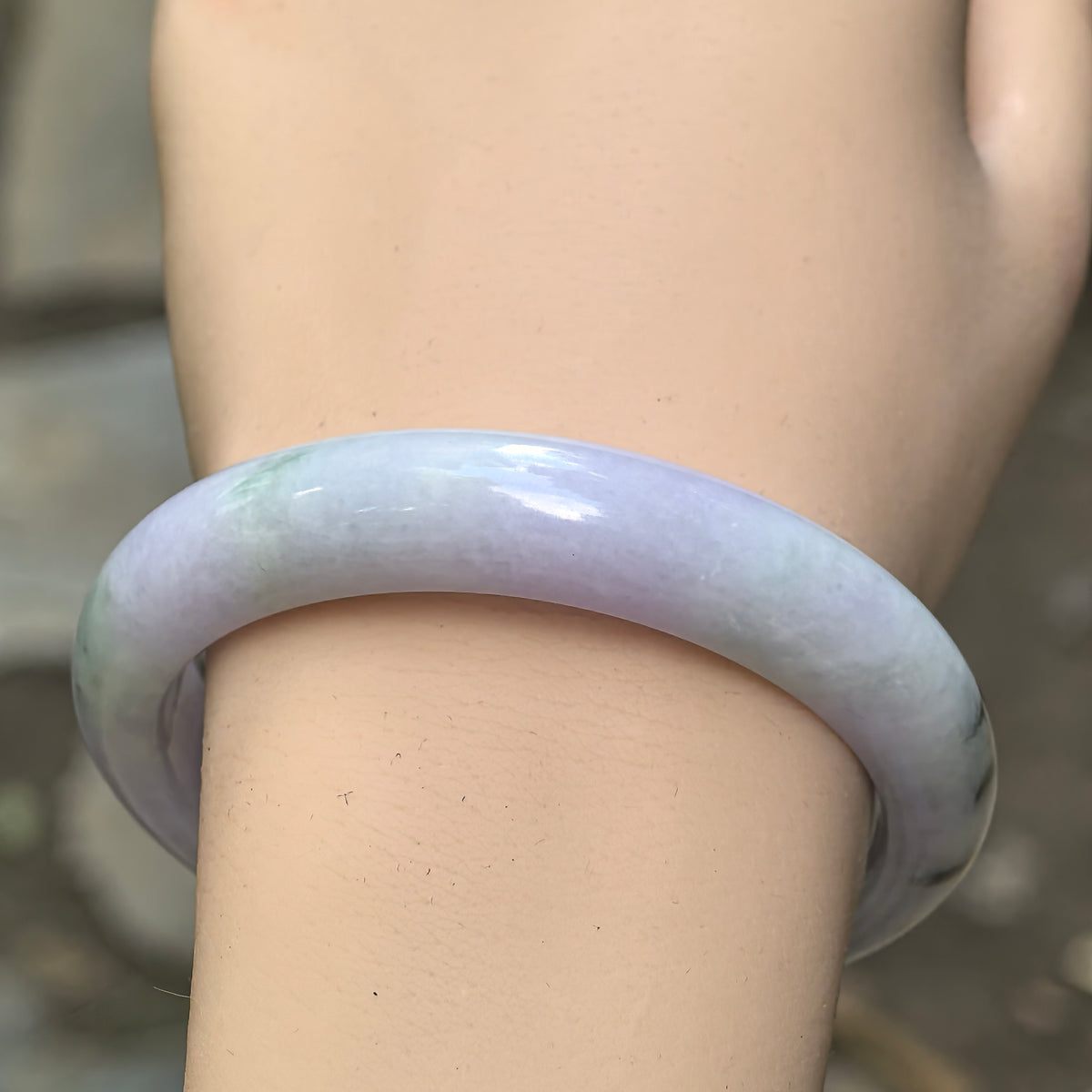 Close-up wrist view of pale lavender and dark green floating flower Burmese jadeite bangle showing its smooth polished surface.