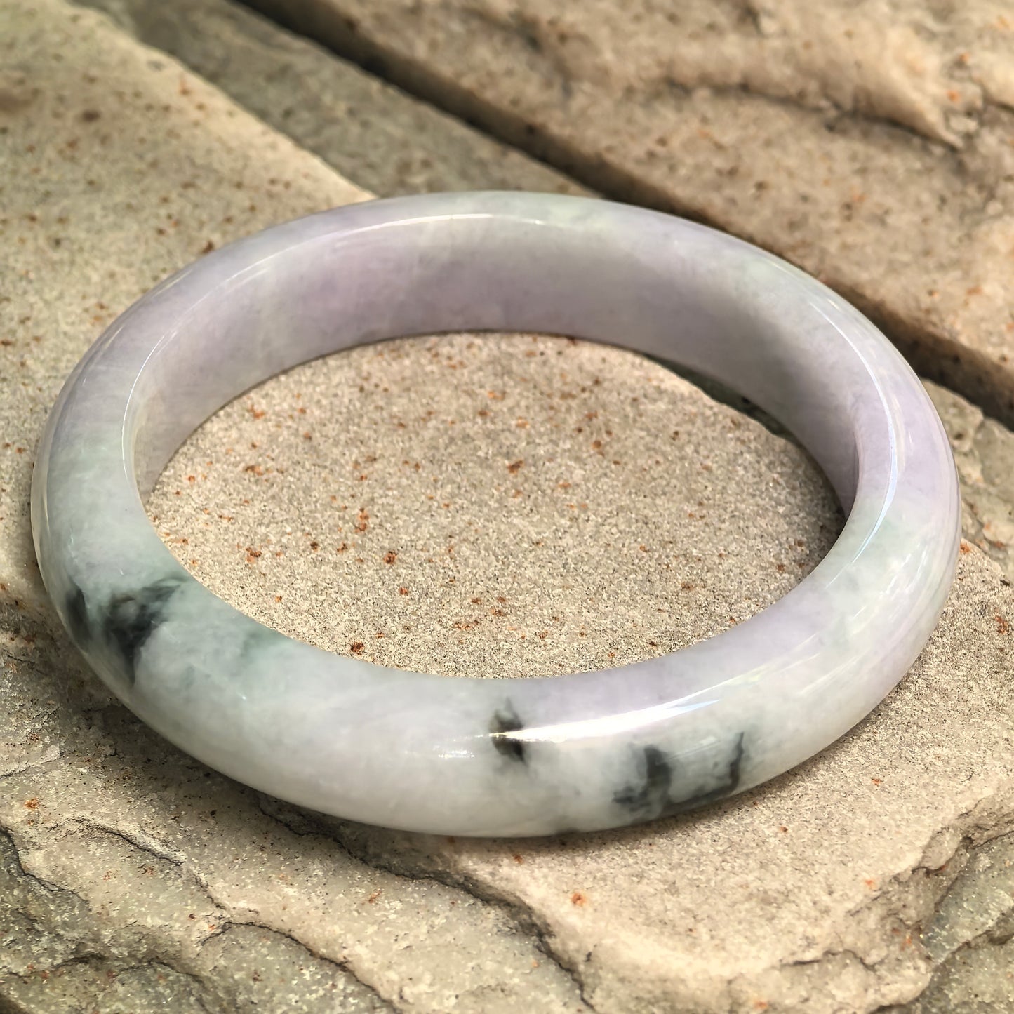 Natural Grade-A glutinous pale lavender jadeite bangle with dark green floating flower displayed on stone.