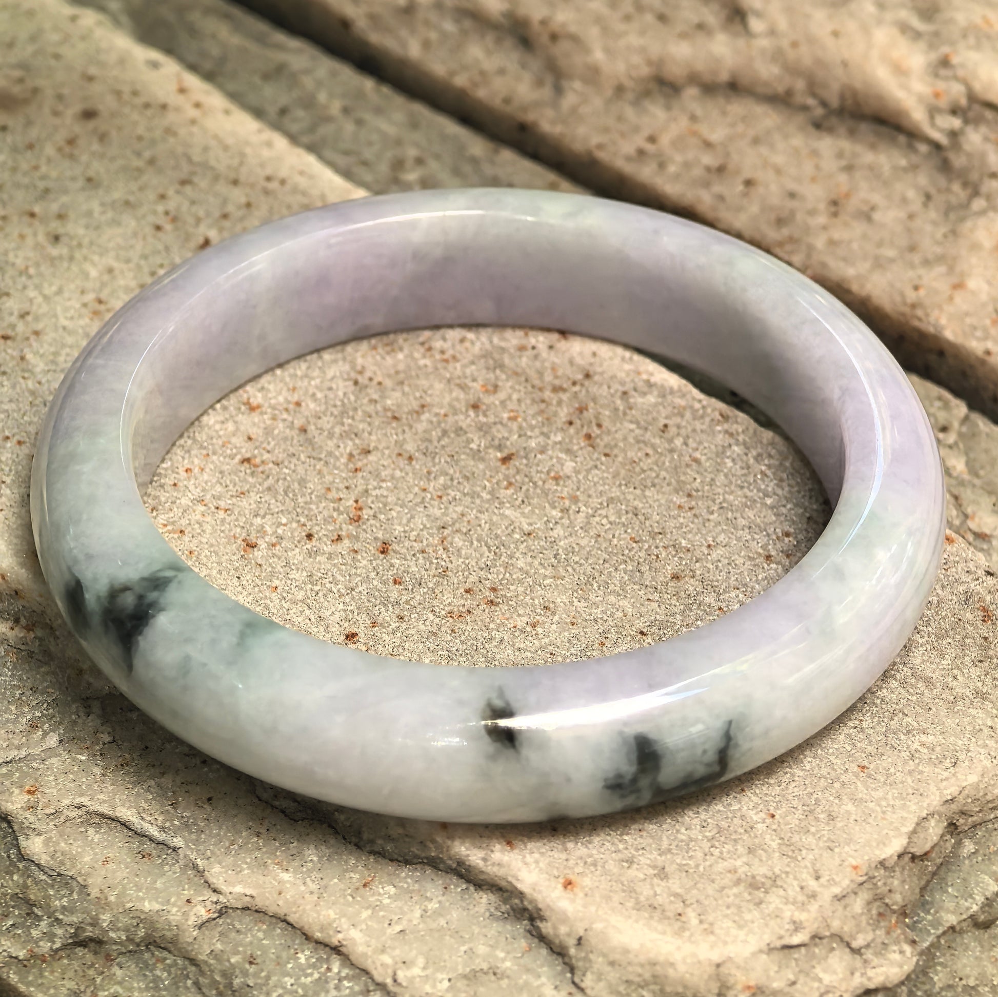 Natural Grade-A glutinous pale lavender jadeite bangle with dark green floating flower displayed on stone.