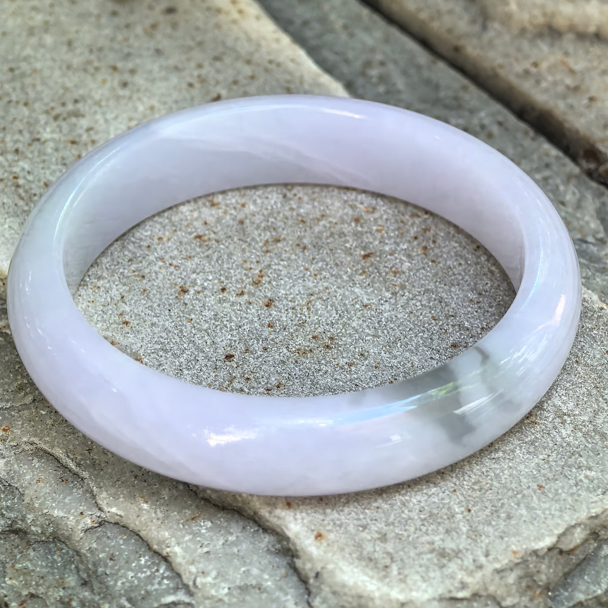 Natural Grade-A glutinous lavender jadeite D-shape bangle shown at an angle with soft translucency and subtle pale green areas.