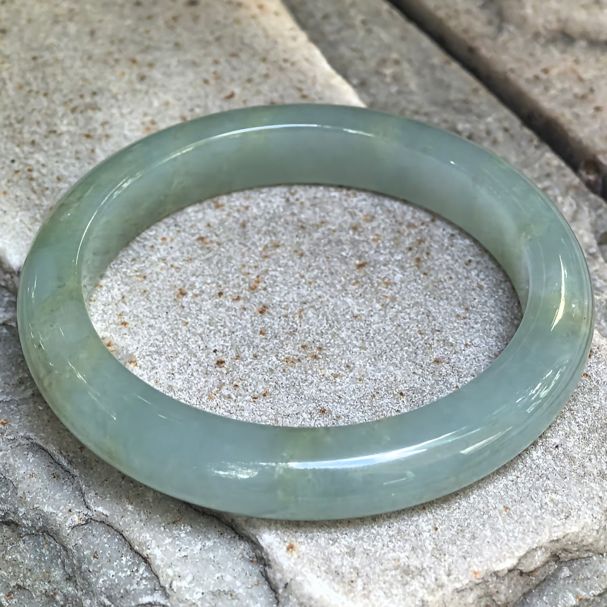 Natural Grade-A icy glutinous mint green D-shape jadeite bangle displayed on stone, showing soft translucency and natural yellow cotton-like inclusions.