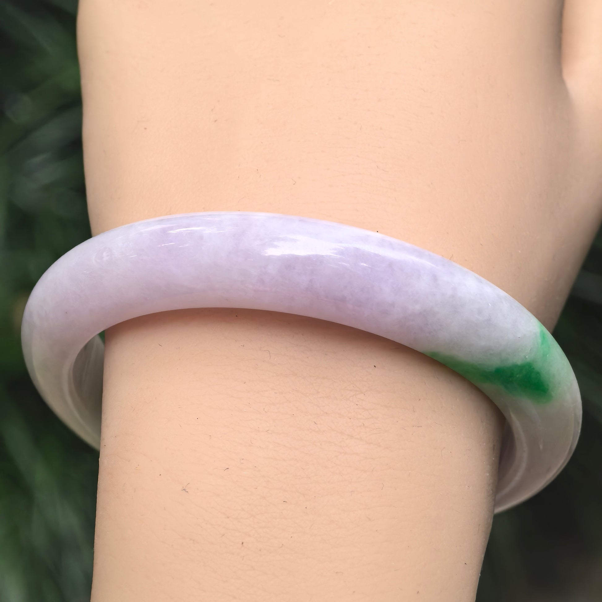 Wrist view of pale lavender Burmese jadeite bangle with vivid green accent and smooth glutinous texture.