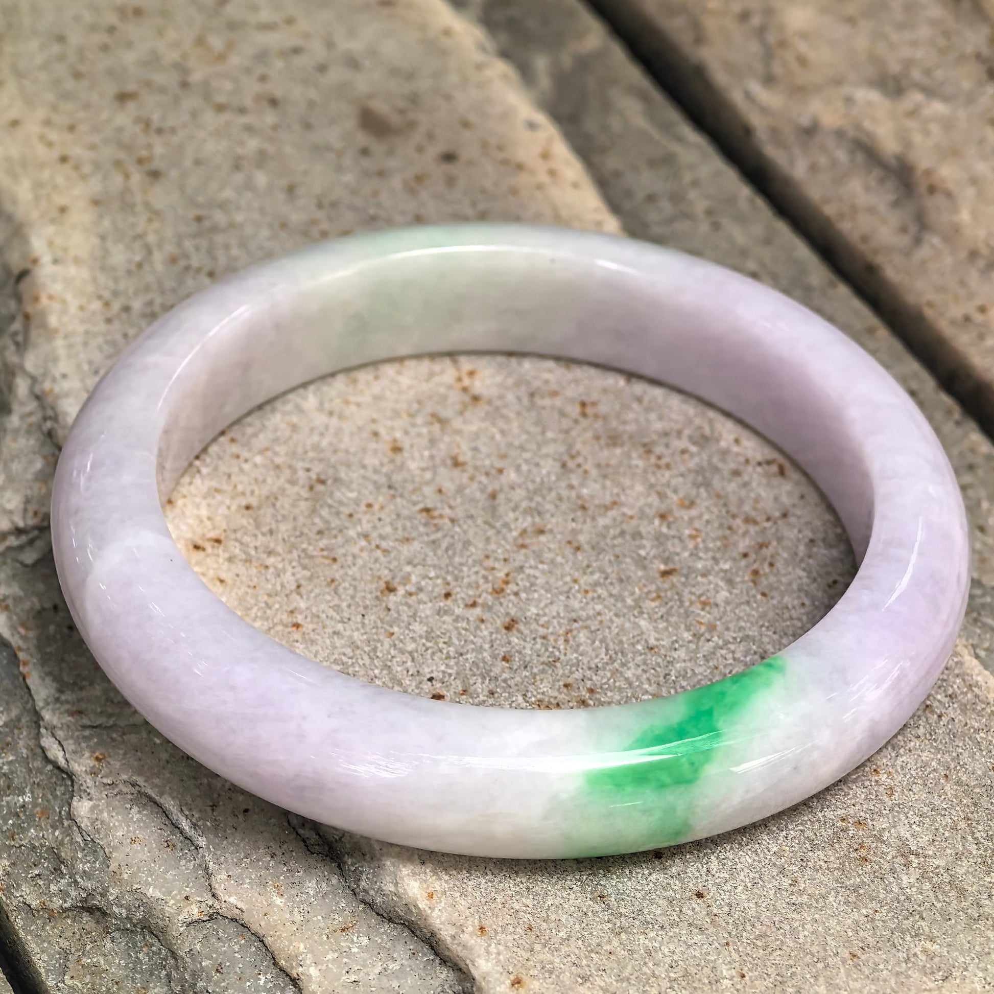Natural Grade-A pale lavender and bright green jadeite D-shape bangle displayed on stone, showing the contrasting color section.