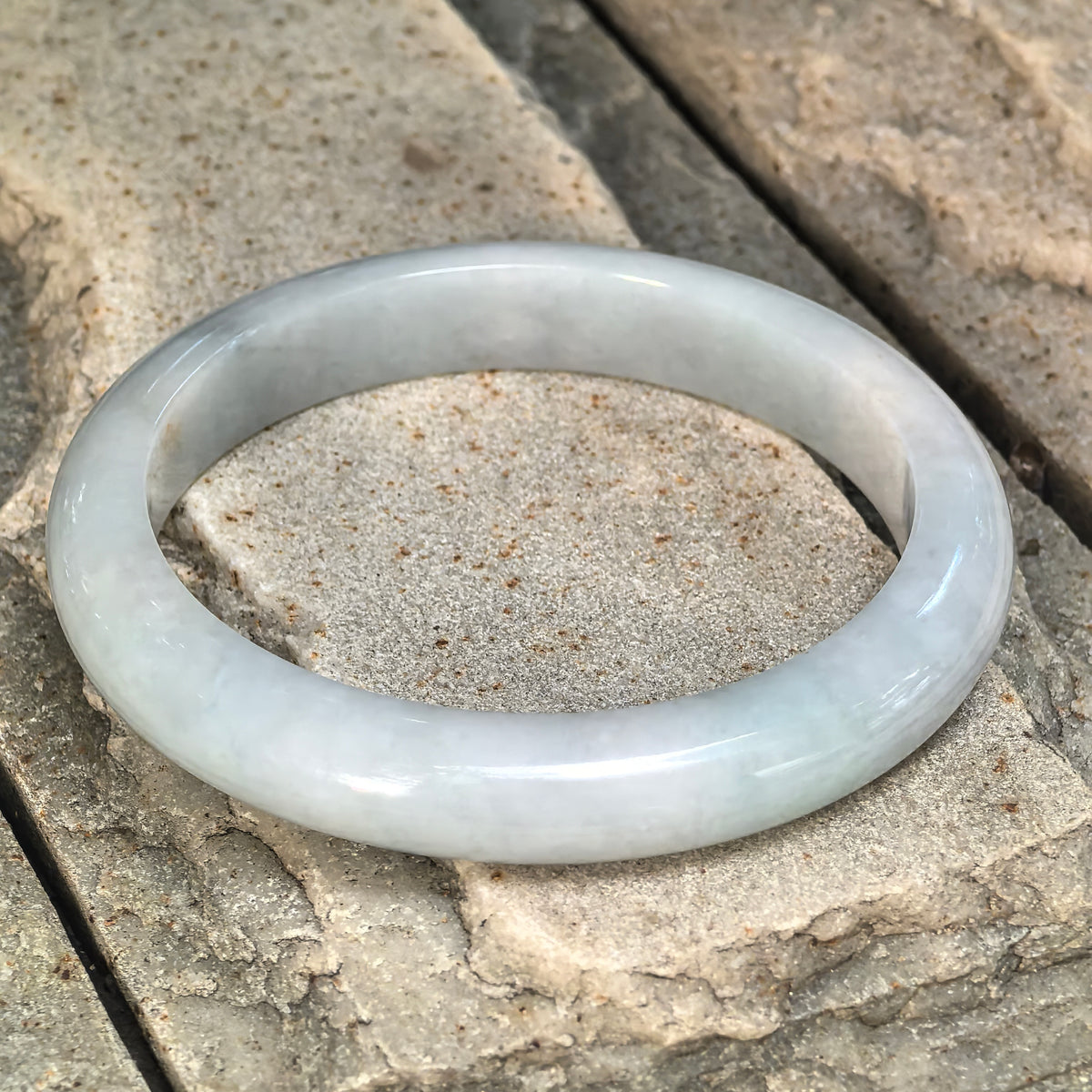Natural Grade-A glutinous pale blue D-shape jadeite bangle displayed on a stone surface.