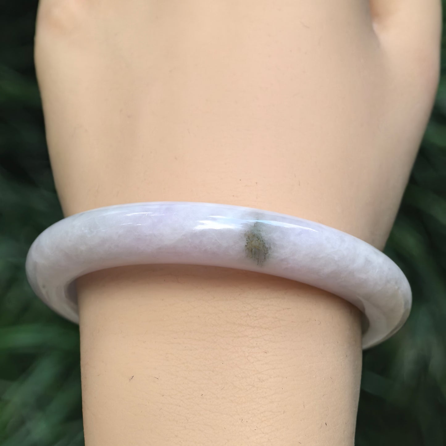 Wrist detail of glutinous pale lavender jadeite bangle showing the dark green floating flower and natural surface condition.
