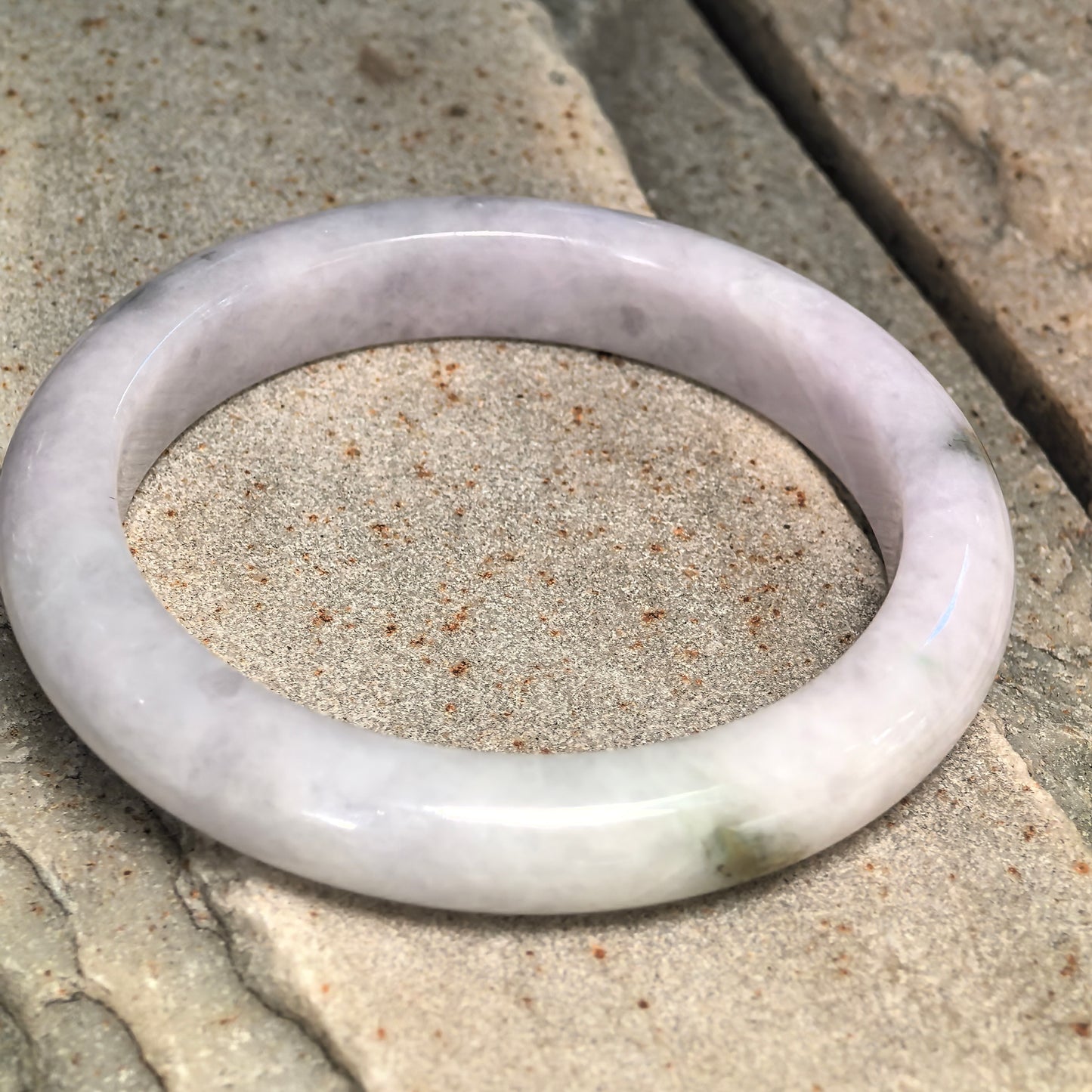 Natural Grade-A glutinous pale lavender D-shape jadeite bangle with dark green floating flower displayed on stone.