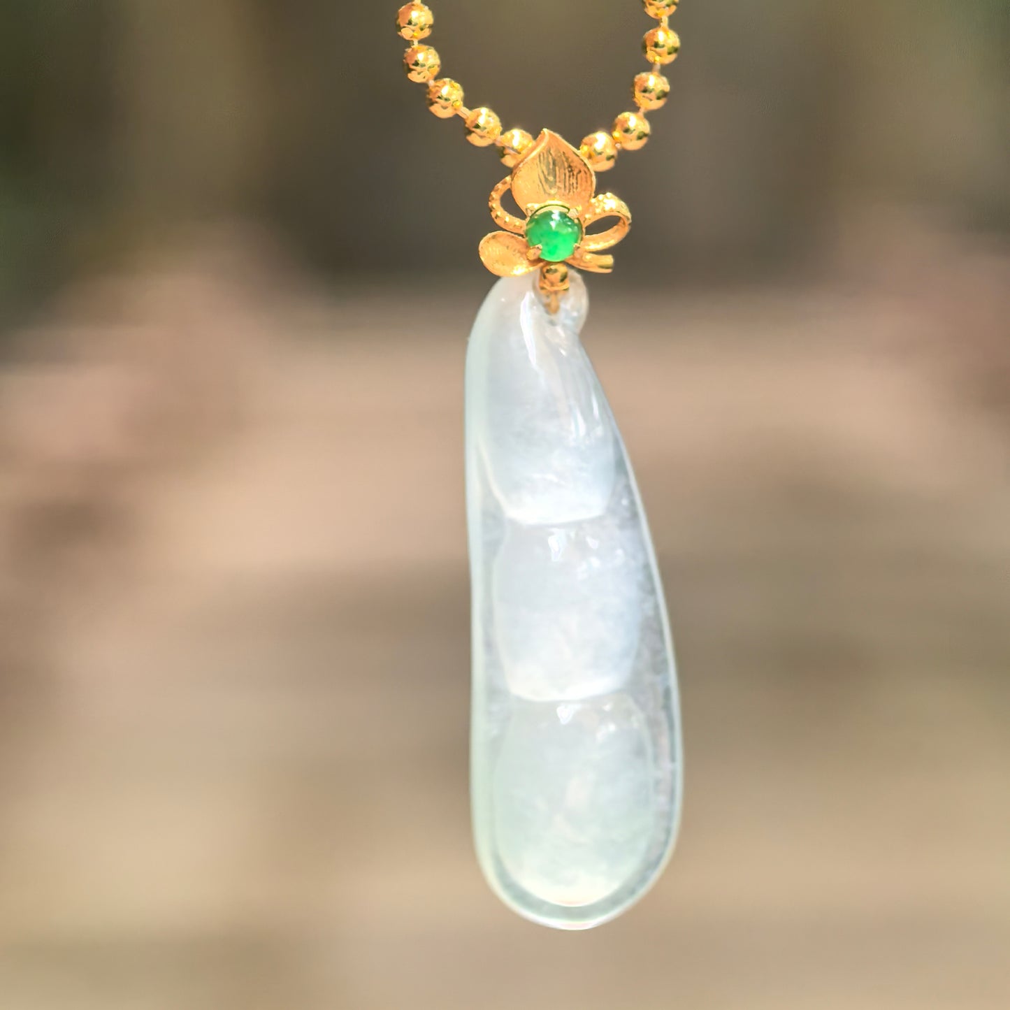 Natural Grade-A icy light green bean pod jadeite pendant hanging from a chain with an 18K gold floral bail.