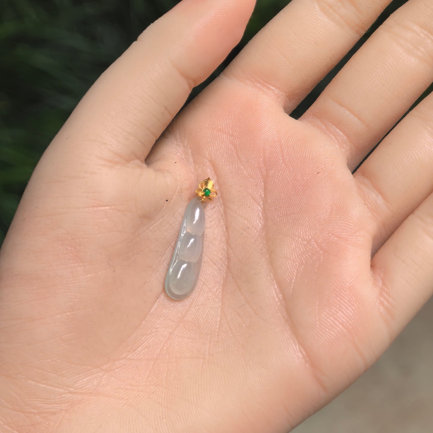 Small icy light green jadeite bean pod pendant shown in hand for scale with polished 18K gold bail.
