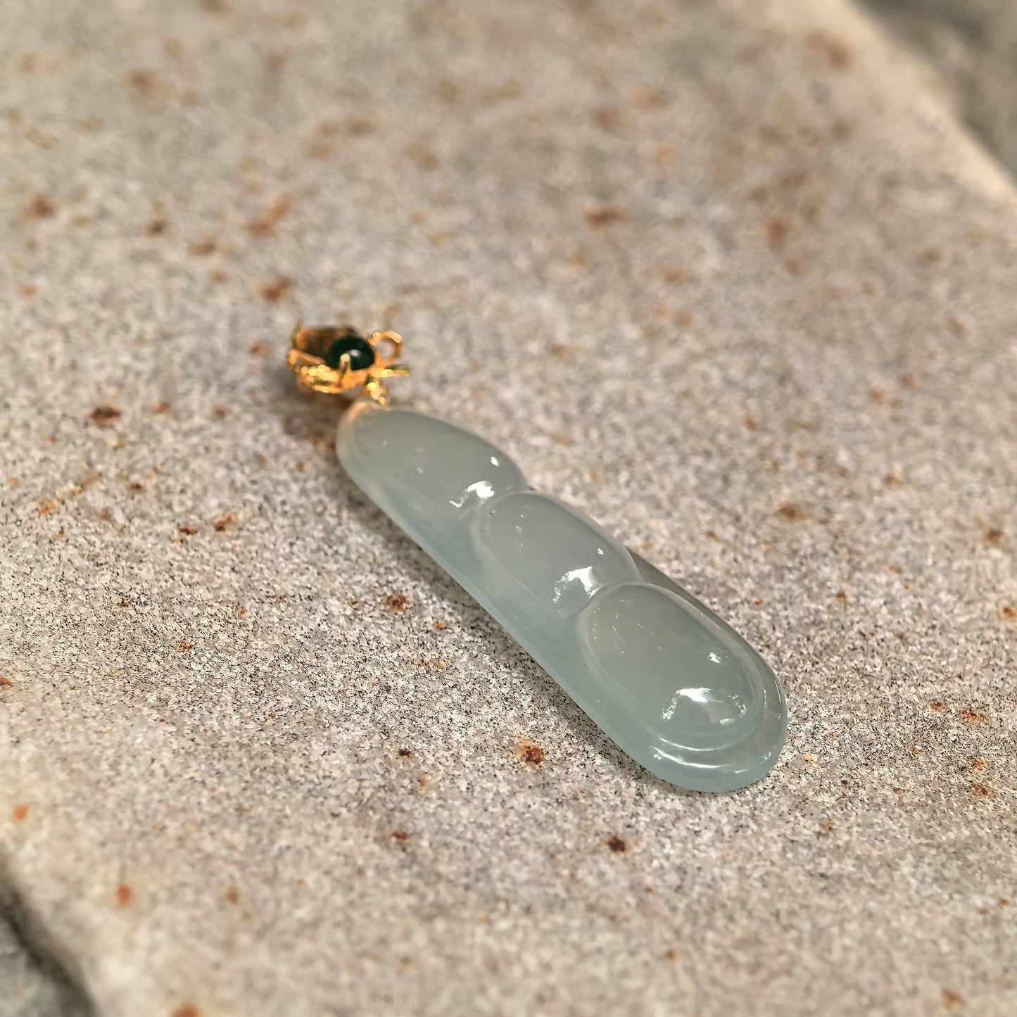 Close-up of light green icy jadeite three-bean pendant showing clean translucent texture and smooth carving.