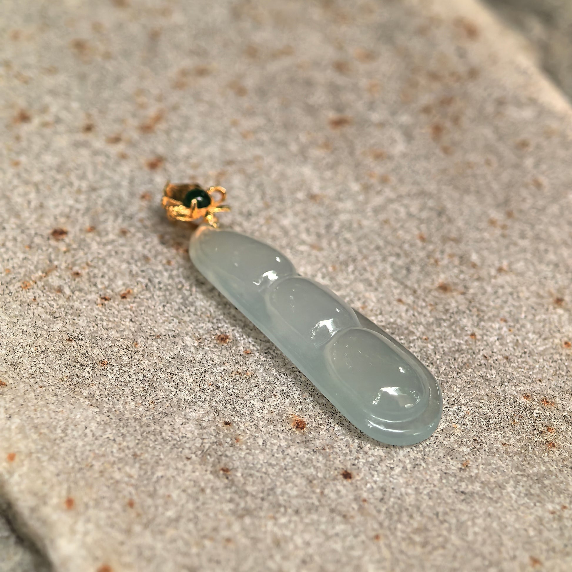 Close-up of light green icy jadeite three-bean pendant showing clean translucent texture and smooth carving.