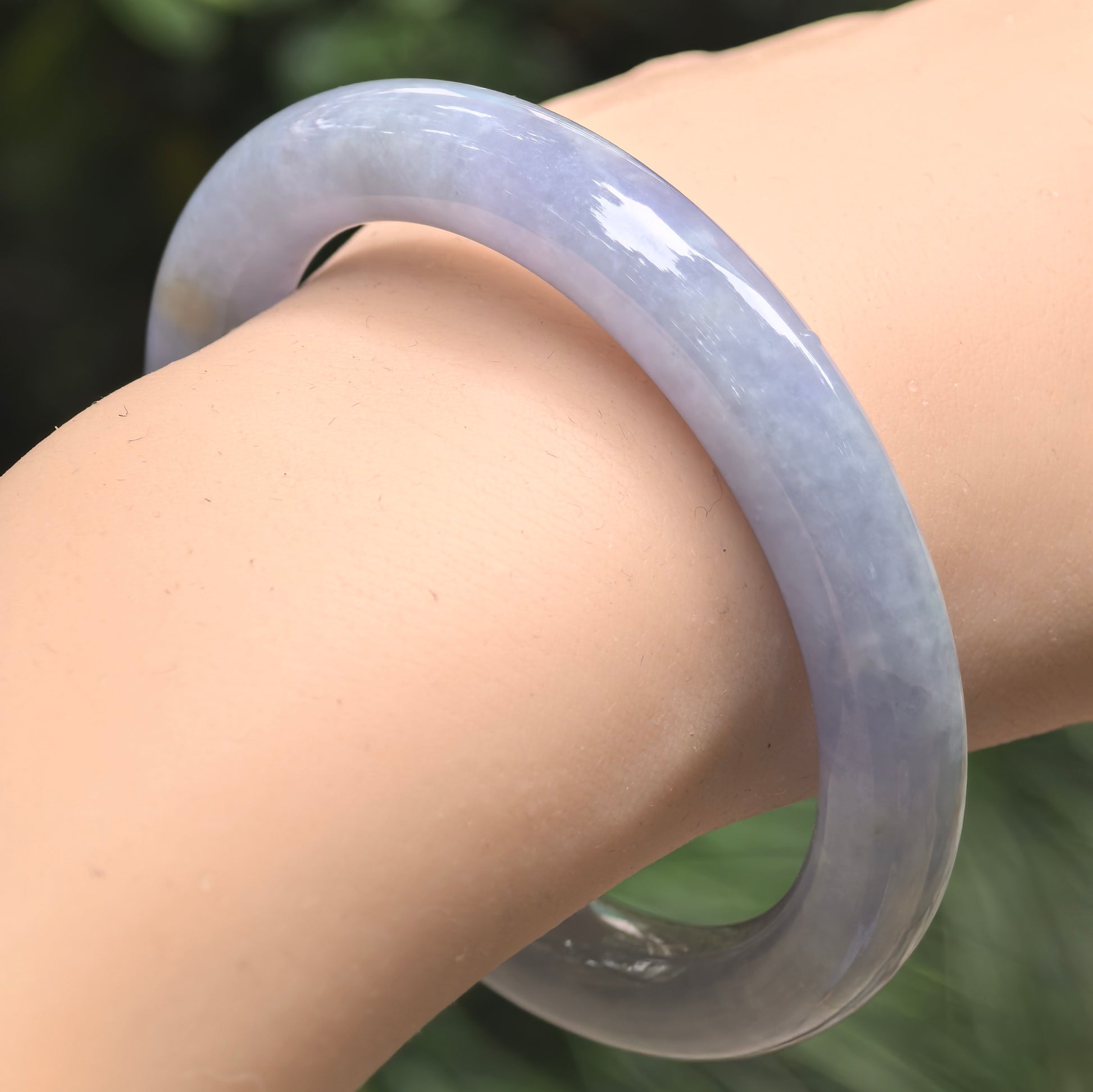 Blue-lavender glutinous jadeite round bangle worn on the wrist, showing its substantial round profile and smooth polished luster.