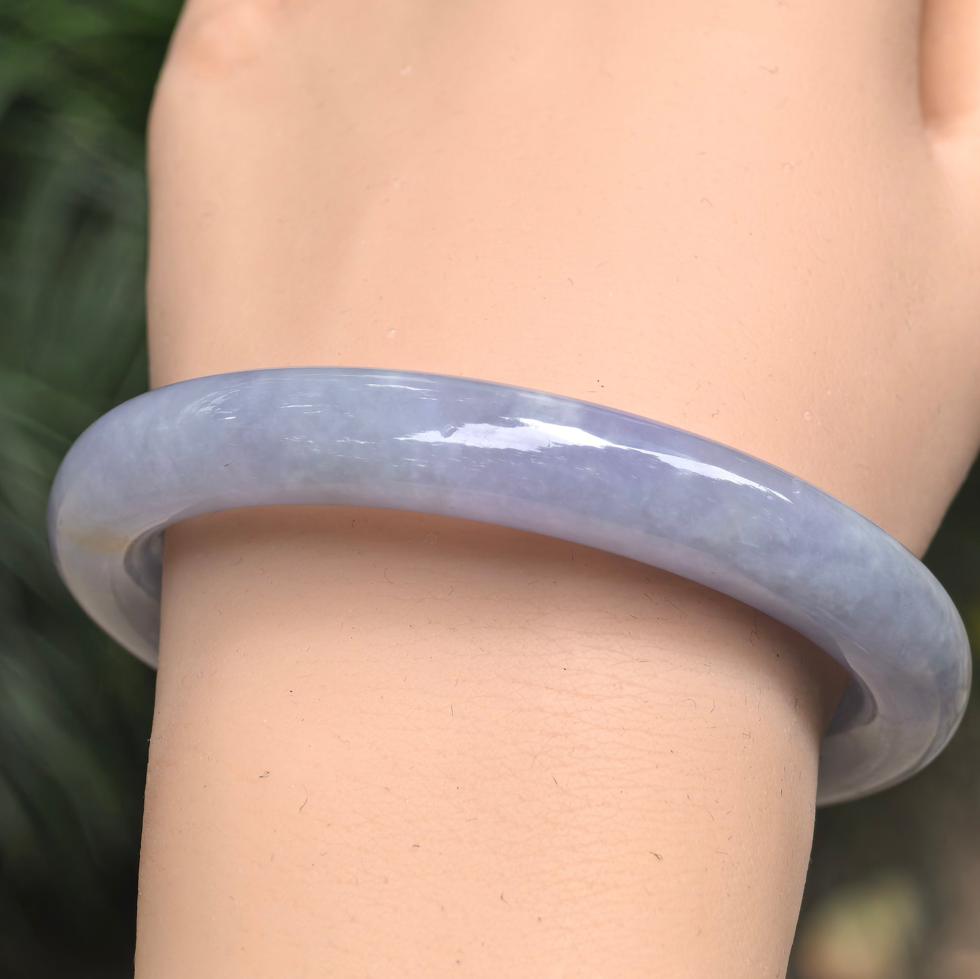 Natural Grade-A Burmese jadeite round bangle worn on the wrist, showing its saturated blue-lavender color under natural light.