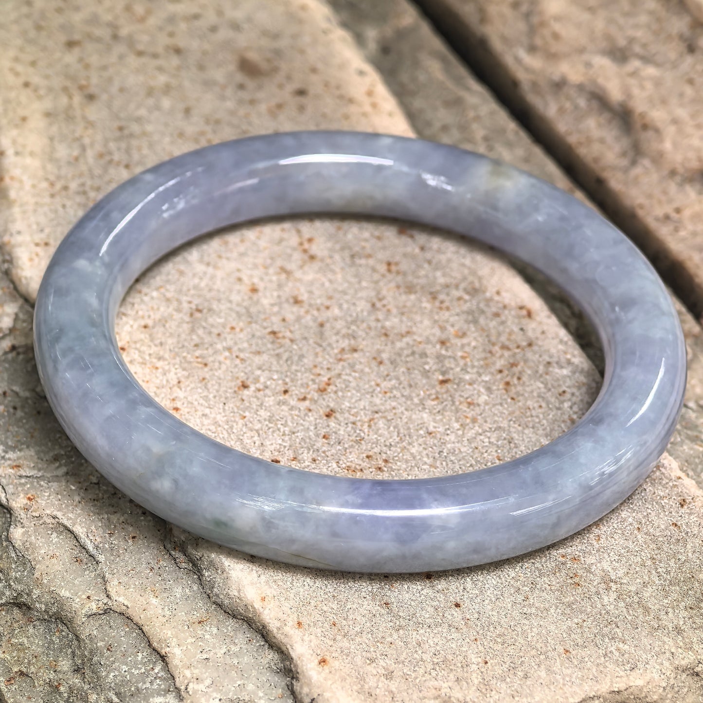 Natural blue-lavender glutinous jadeite round bangle displayed flat, showing the rich cool-toned color and polished surface.