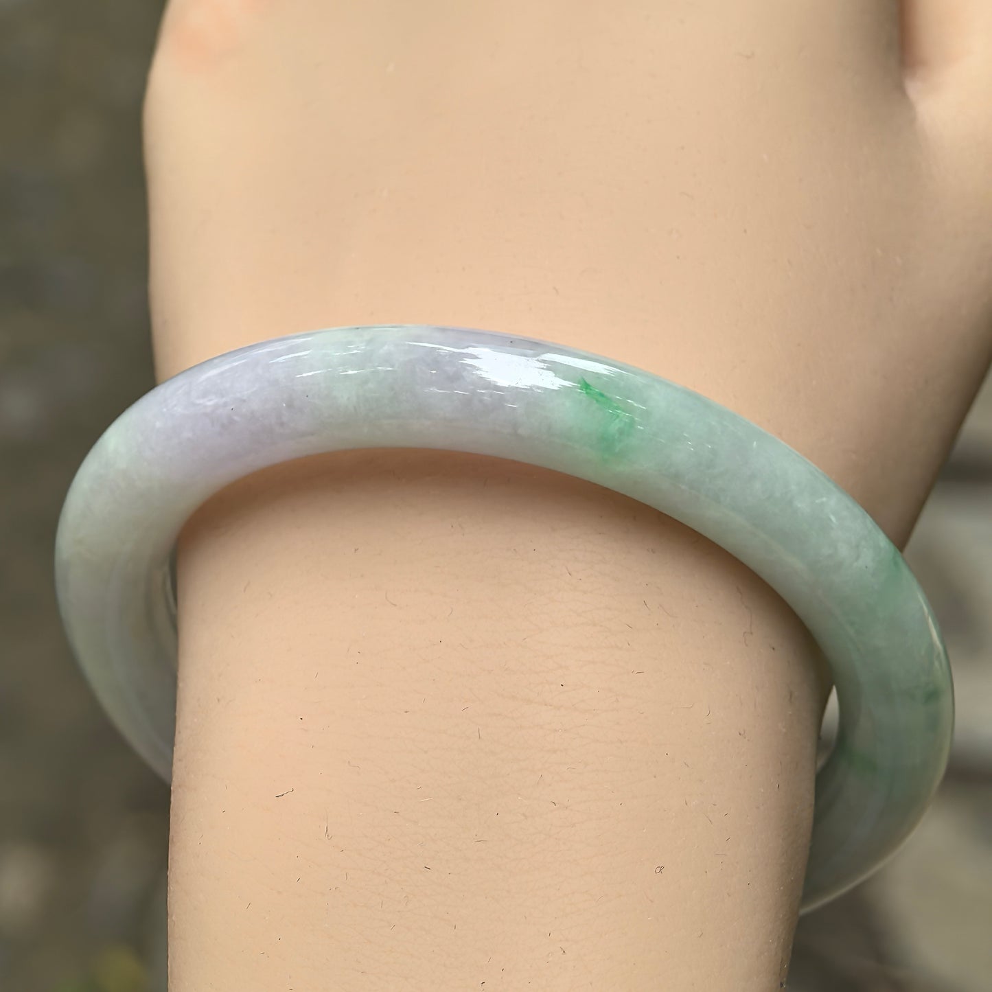 Wrist view of natural pale lavender and green Burmese jadeite round bangle showing the soft color transition and smooth luster.