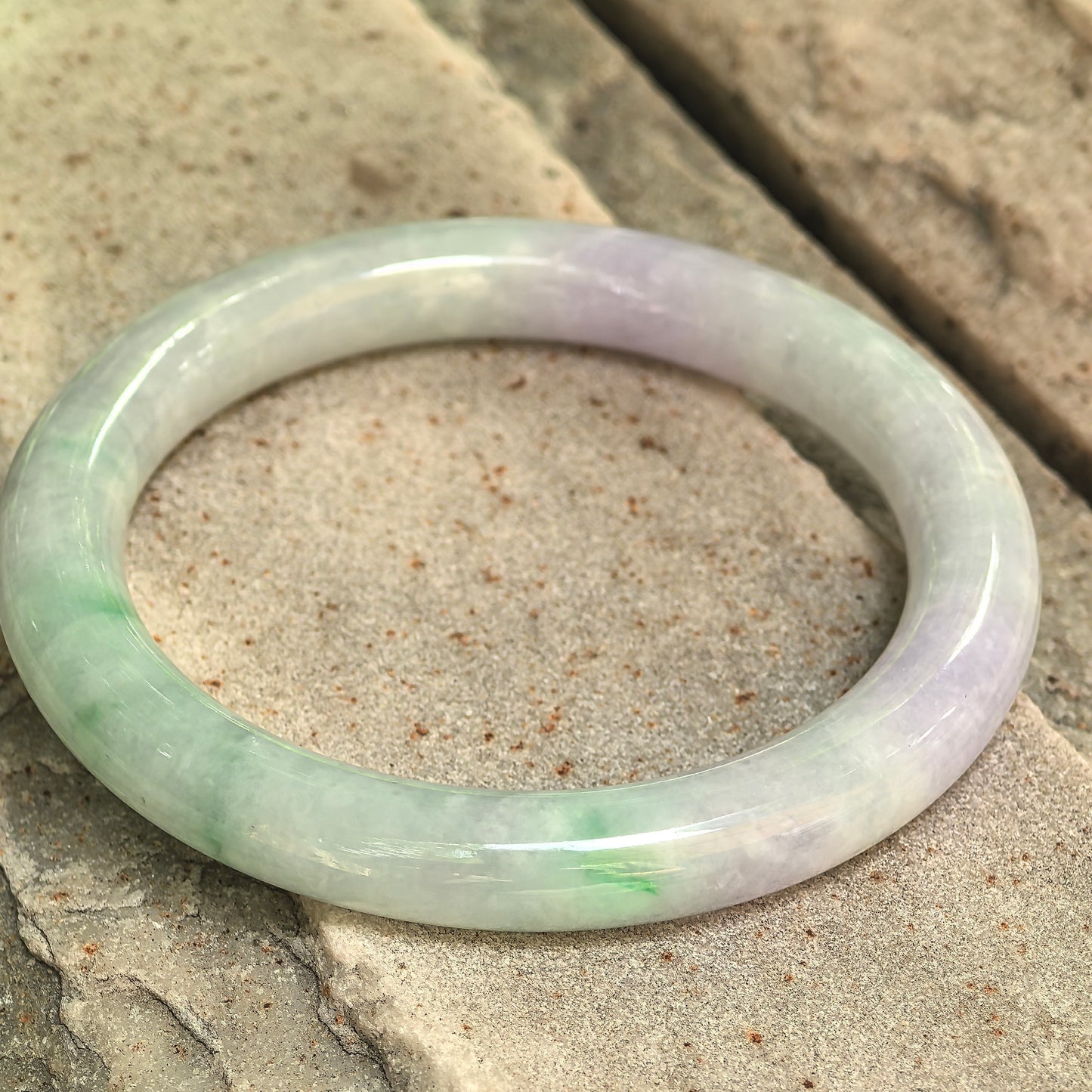Natural Grade-A glutinous lavender-green jadeite round bangle displayed on stone, showing its polished surface and mixed colors.